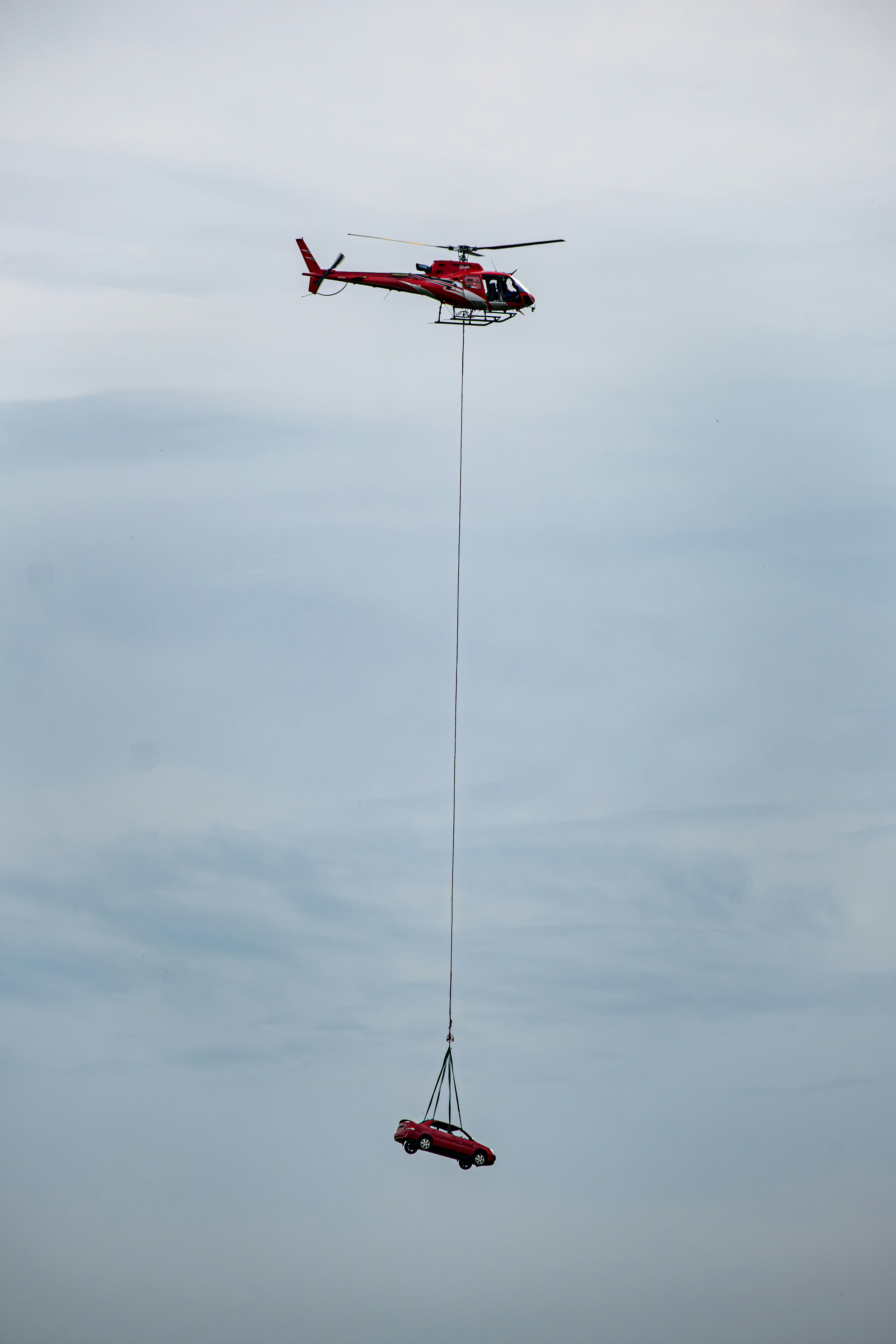 Helicóptero vermelho levantando um carro vermelho contra um céu nublado.