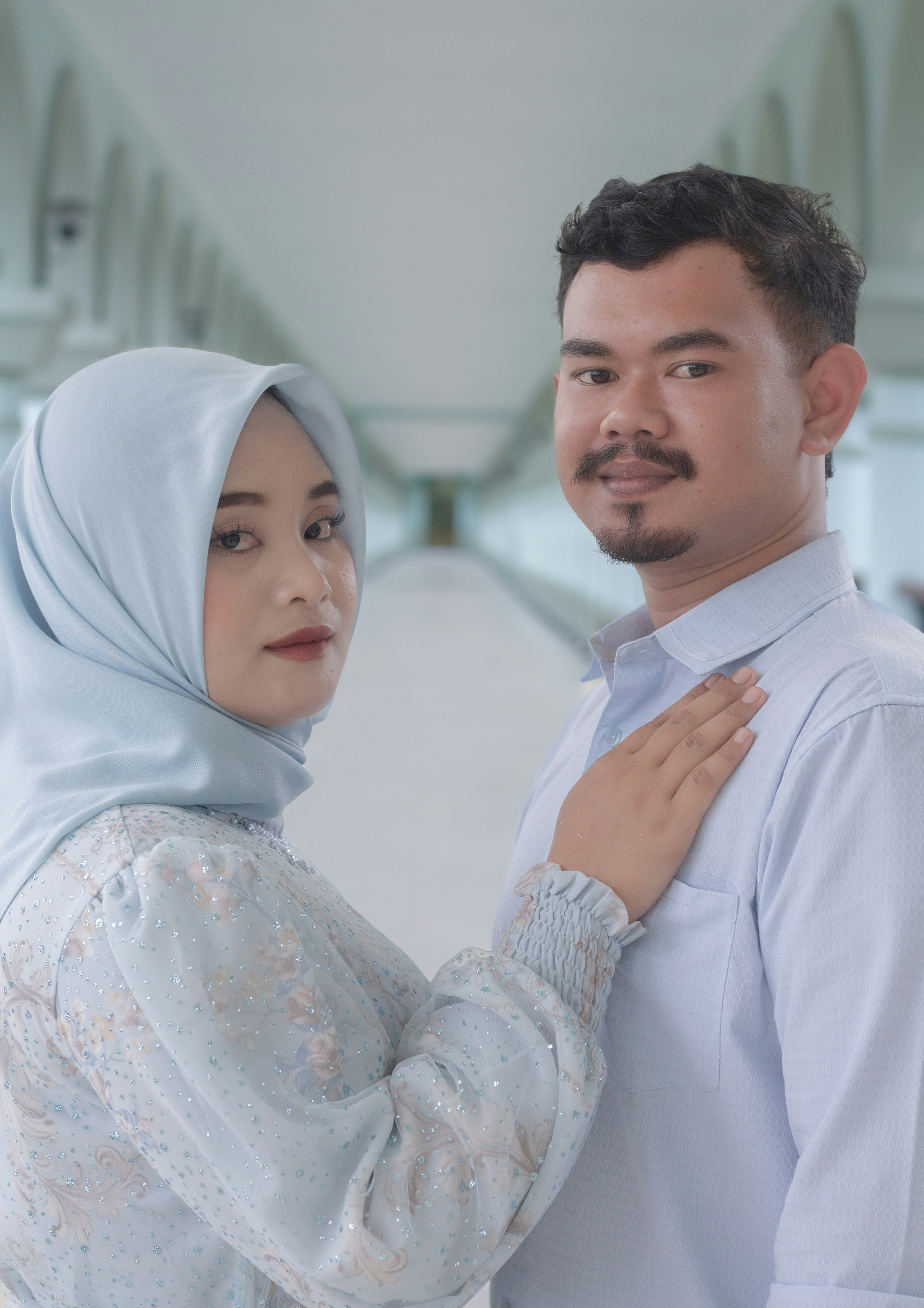 Sepasang suami istri berpakaian biru muda berpose di lorong.