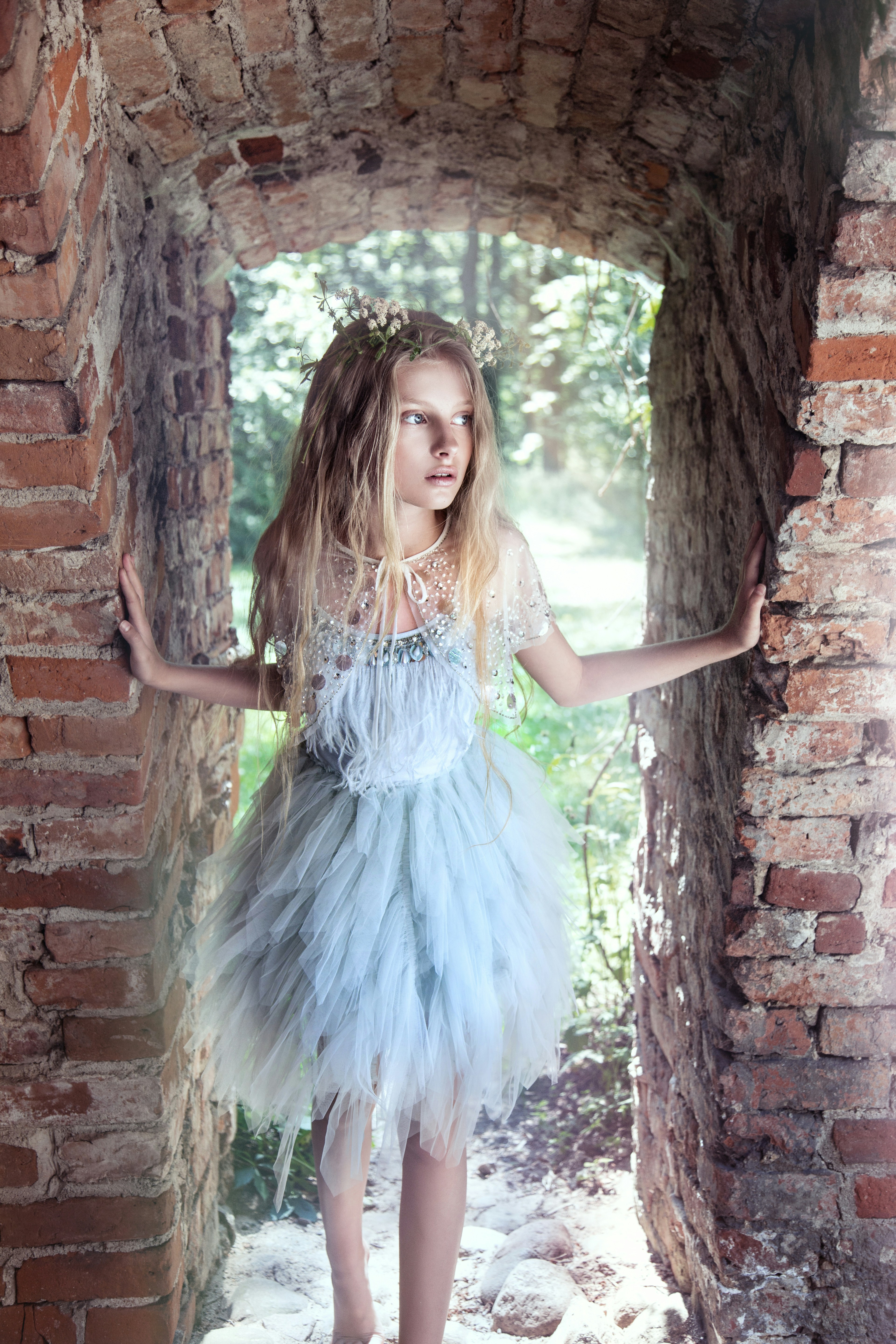 Chica rubia con vestido azul de plumas en un antiguo arco de ladrillo