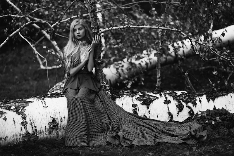 woman in flowing dress by a fallen birch tree
