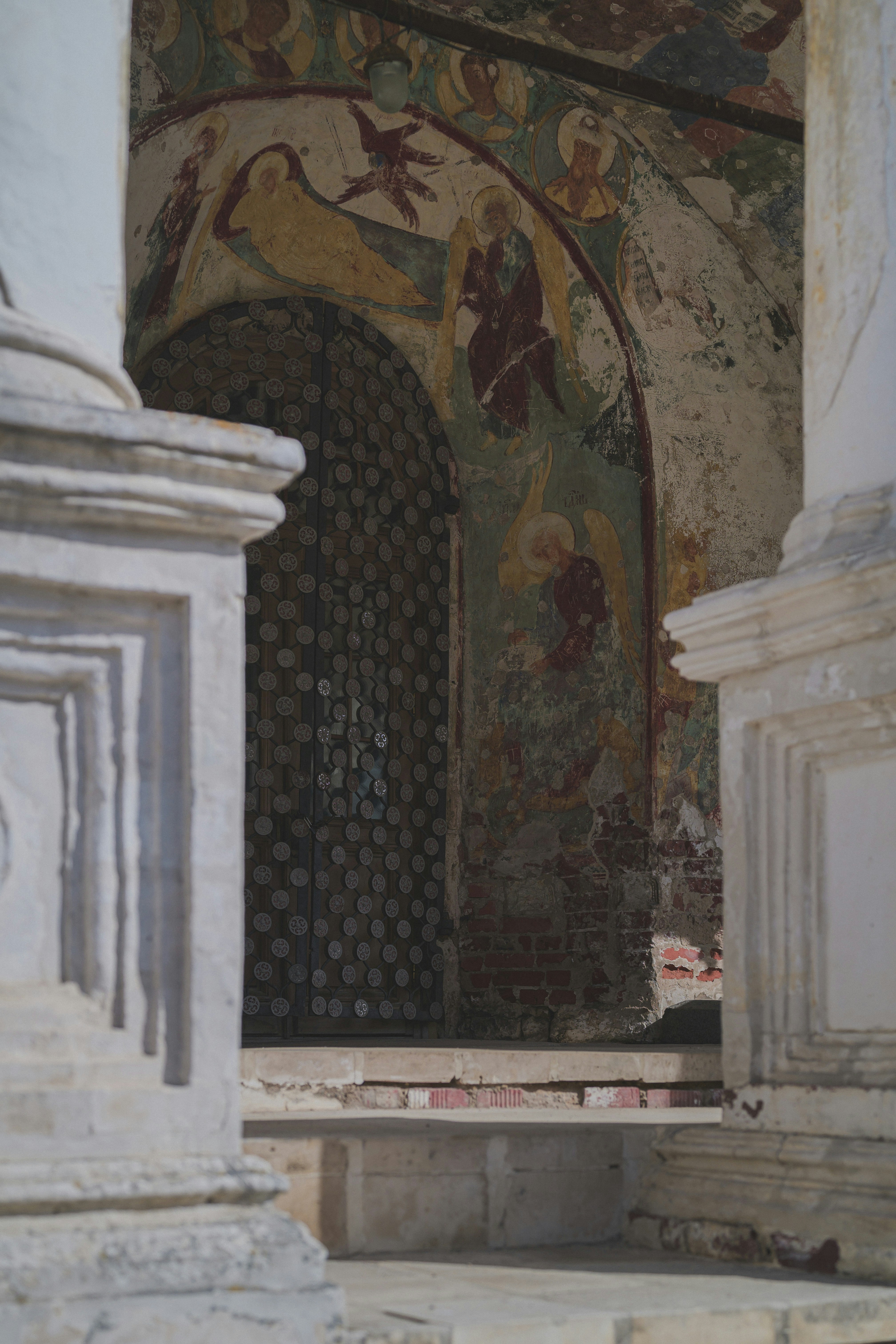 Ancient frescoes adorn a church archway with a metal grate.