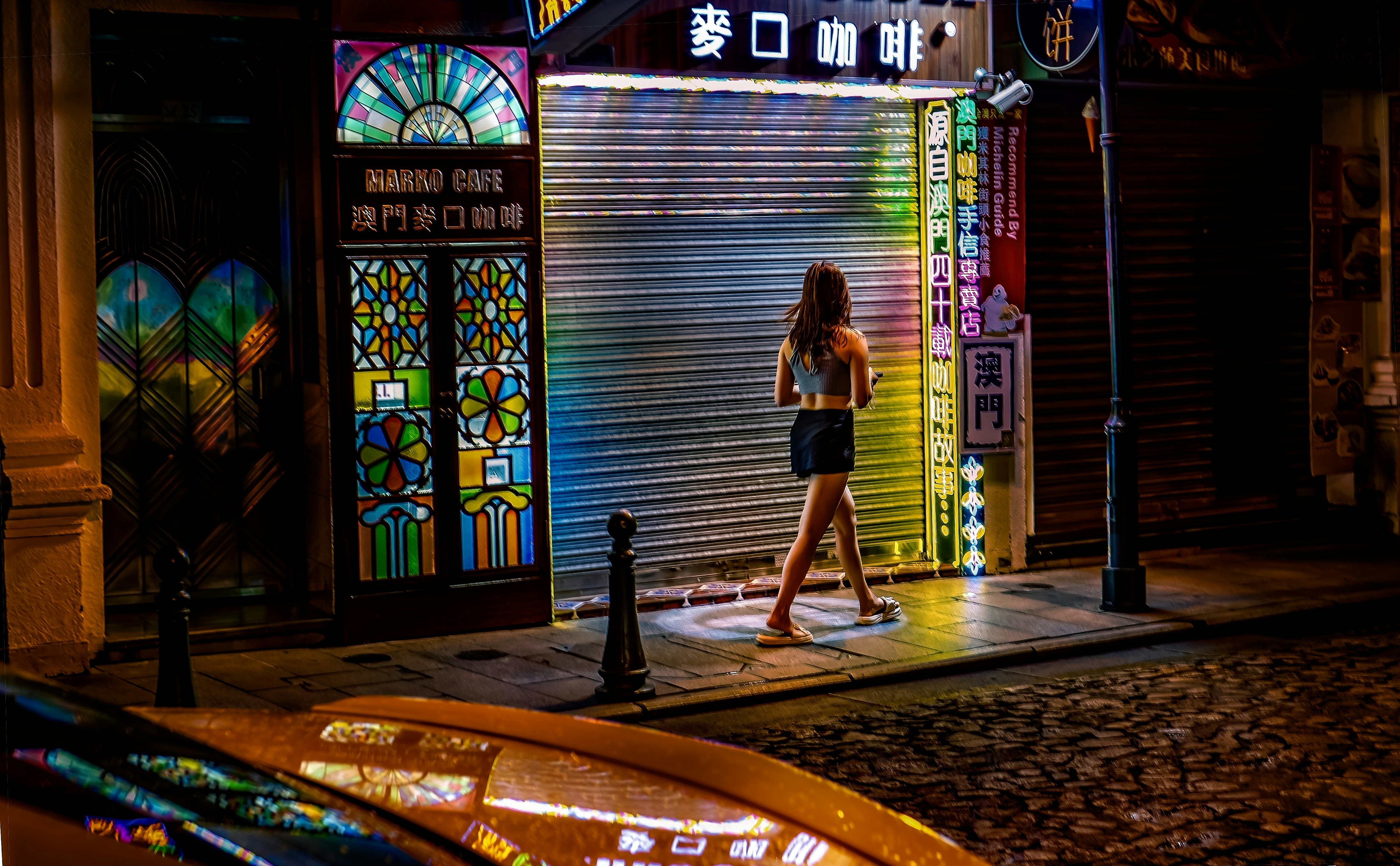 Una mujer camina por una calle colorida iluminada con neones de noche.