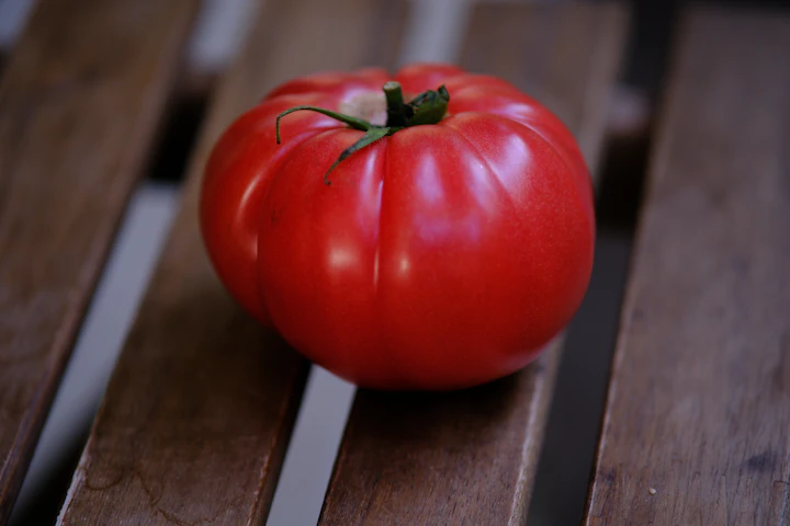 A single ripe red tomato on a wooden surface