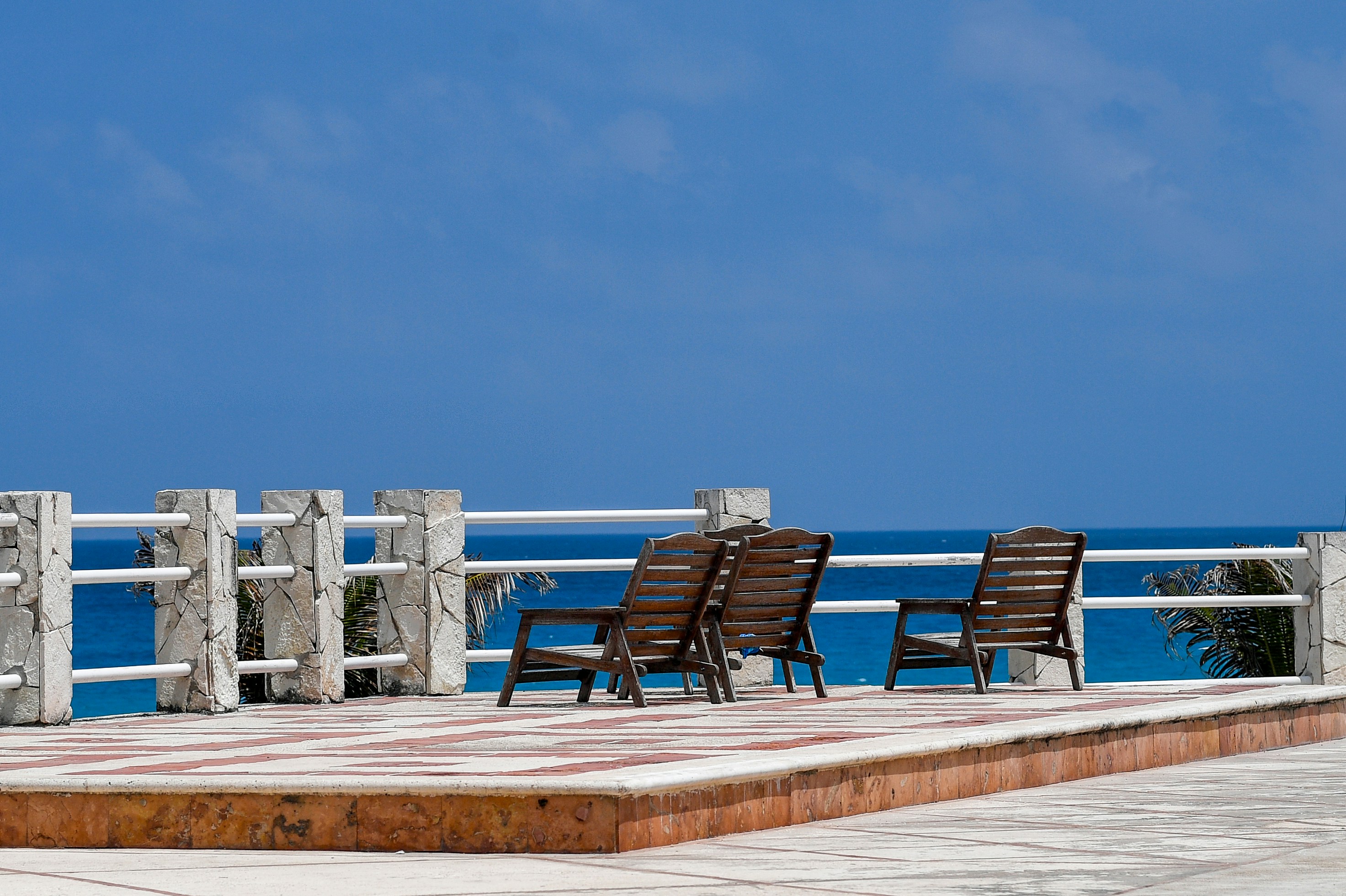 Two wooden chairs on a patio overlooking the blue ocean.