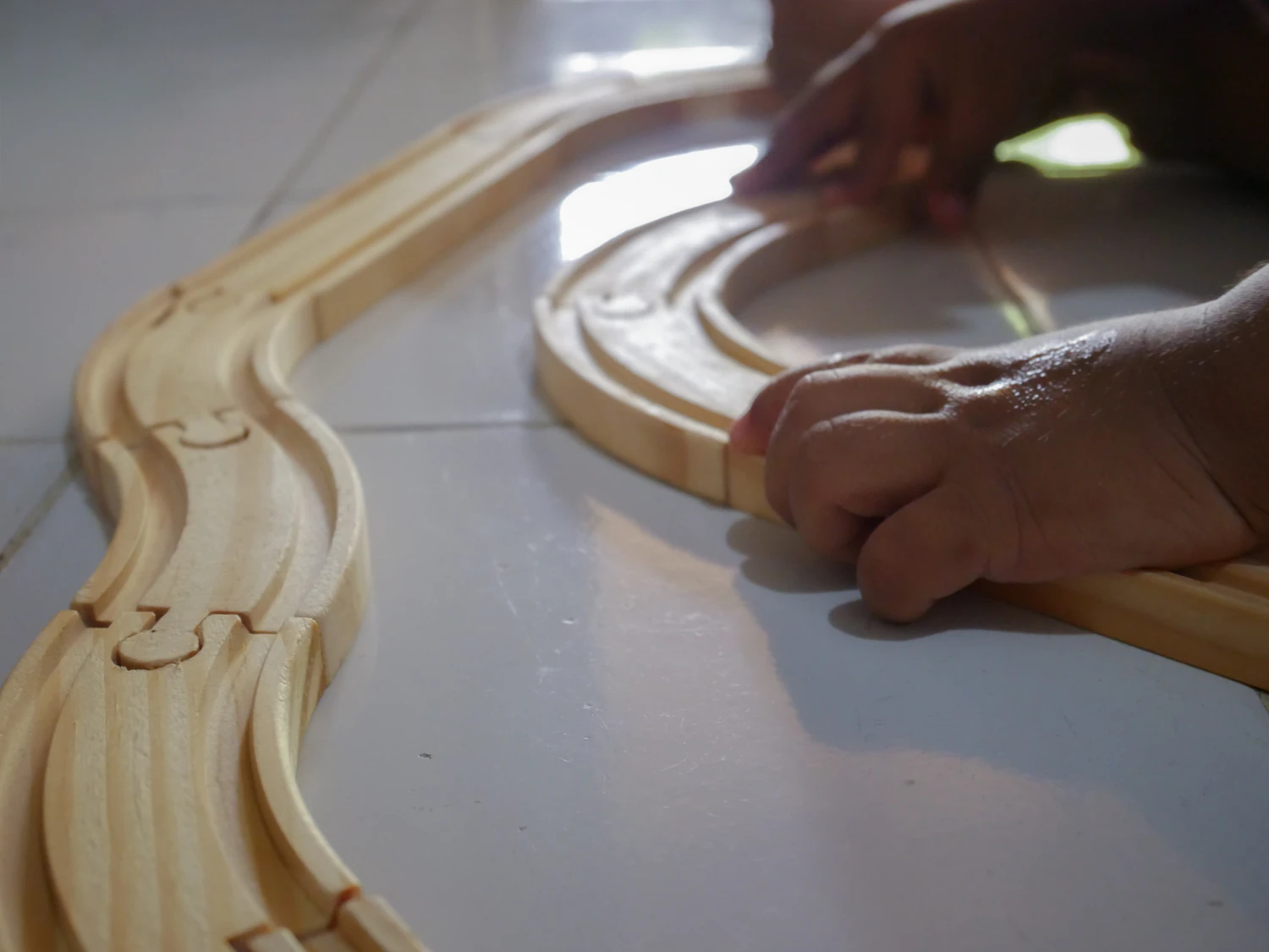 A child's hands laying curved wooden train track across a pale floor — Lakeside Track Loop, in stock