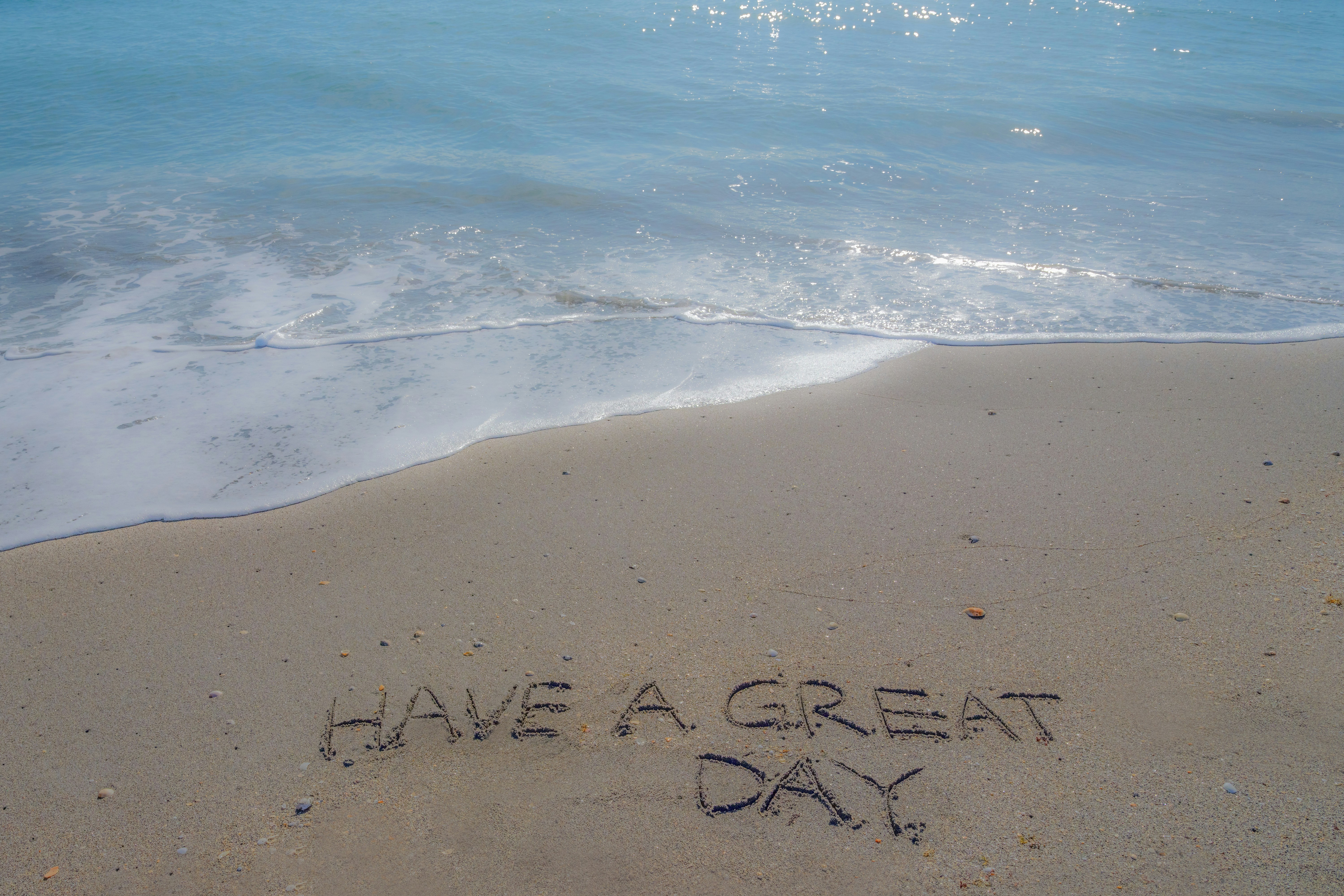 “have a great day” written in sand with ocean waves.