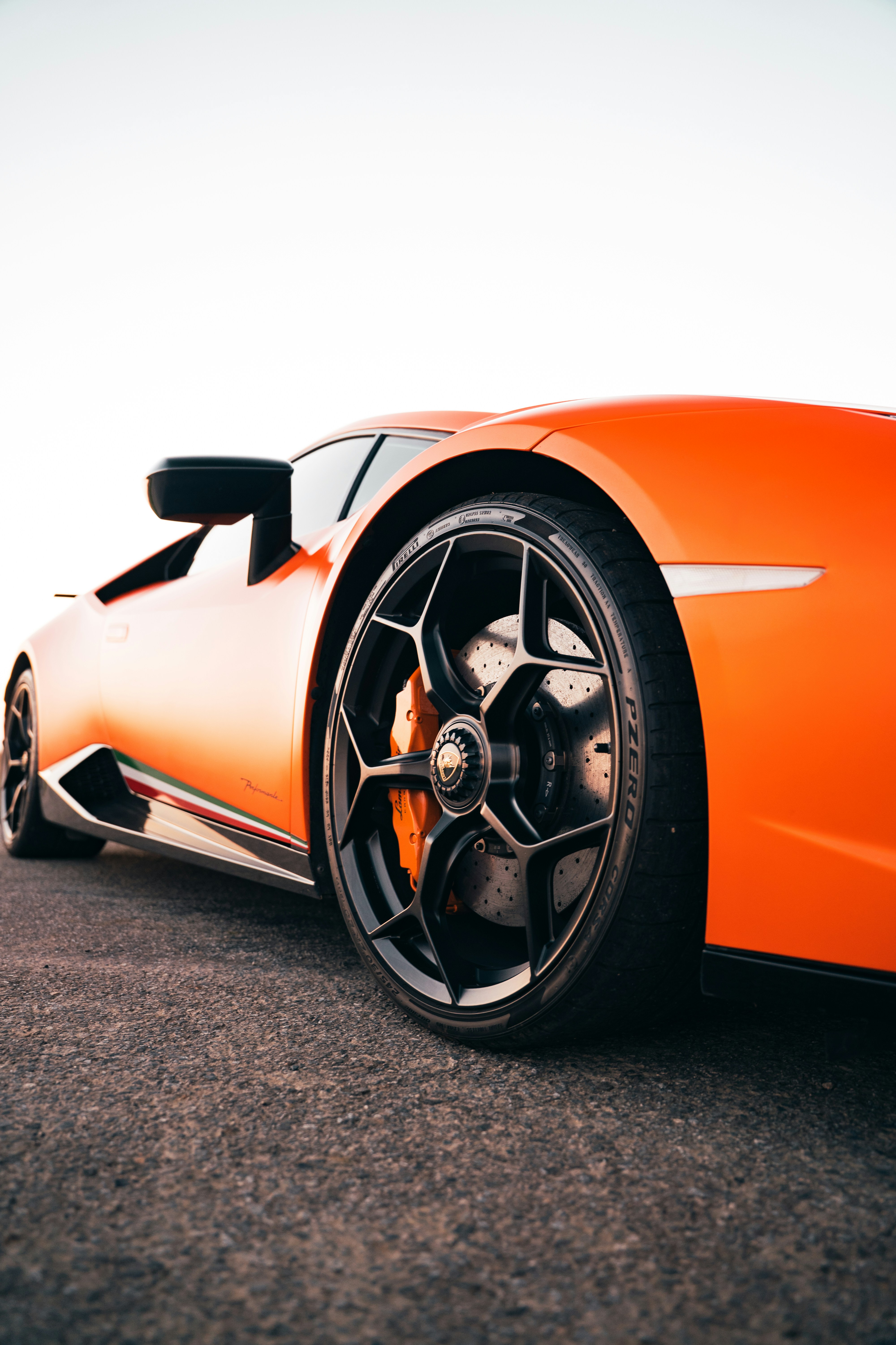 An orange sports car with a black wheel on asphalt.