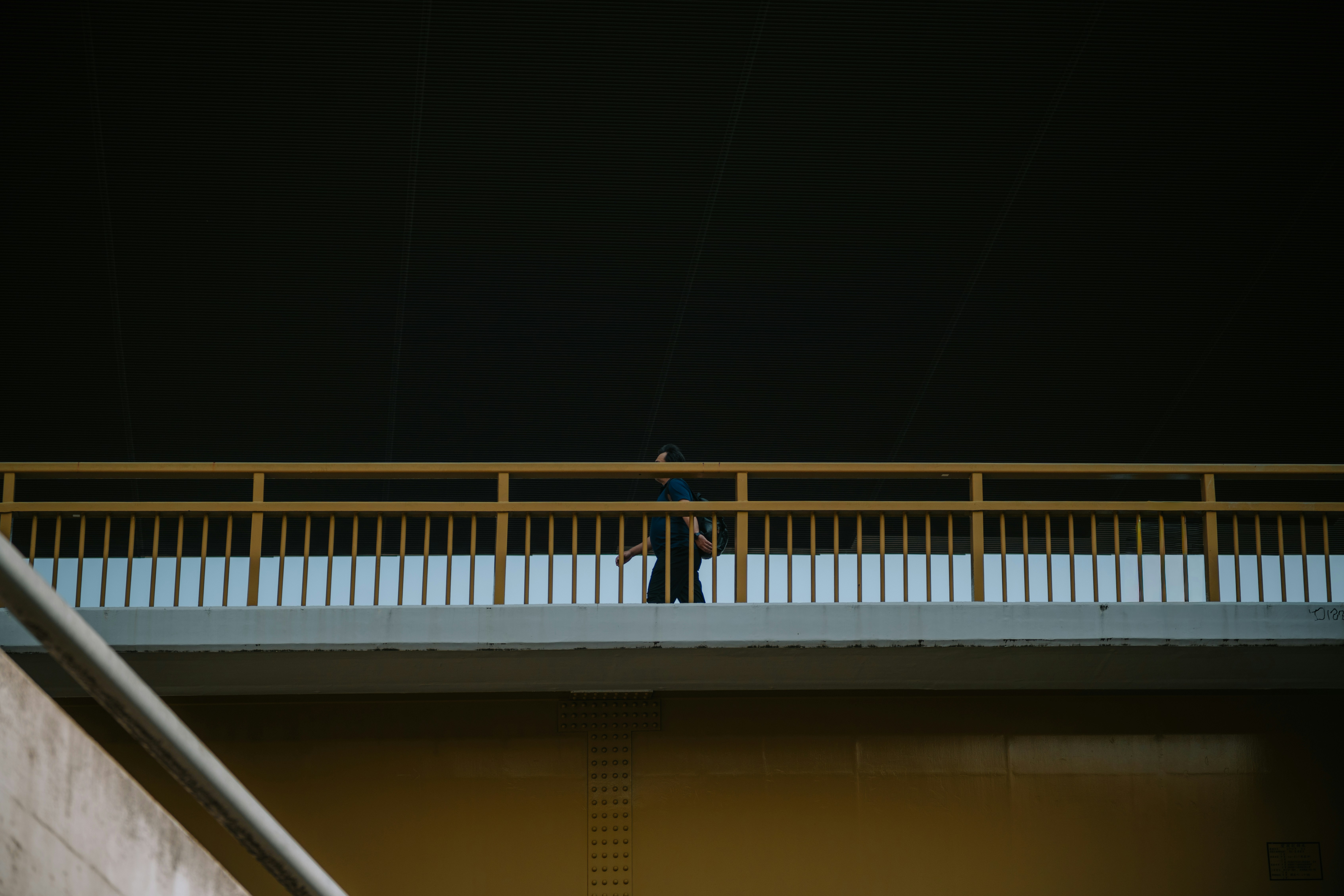 Person walking on a bridge with yellow railings at night.