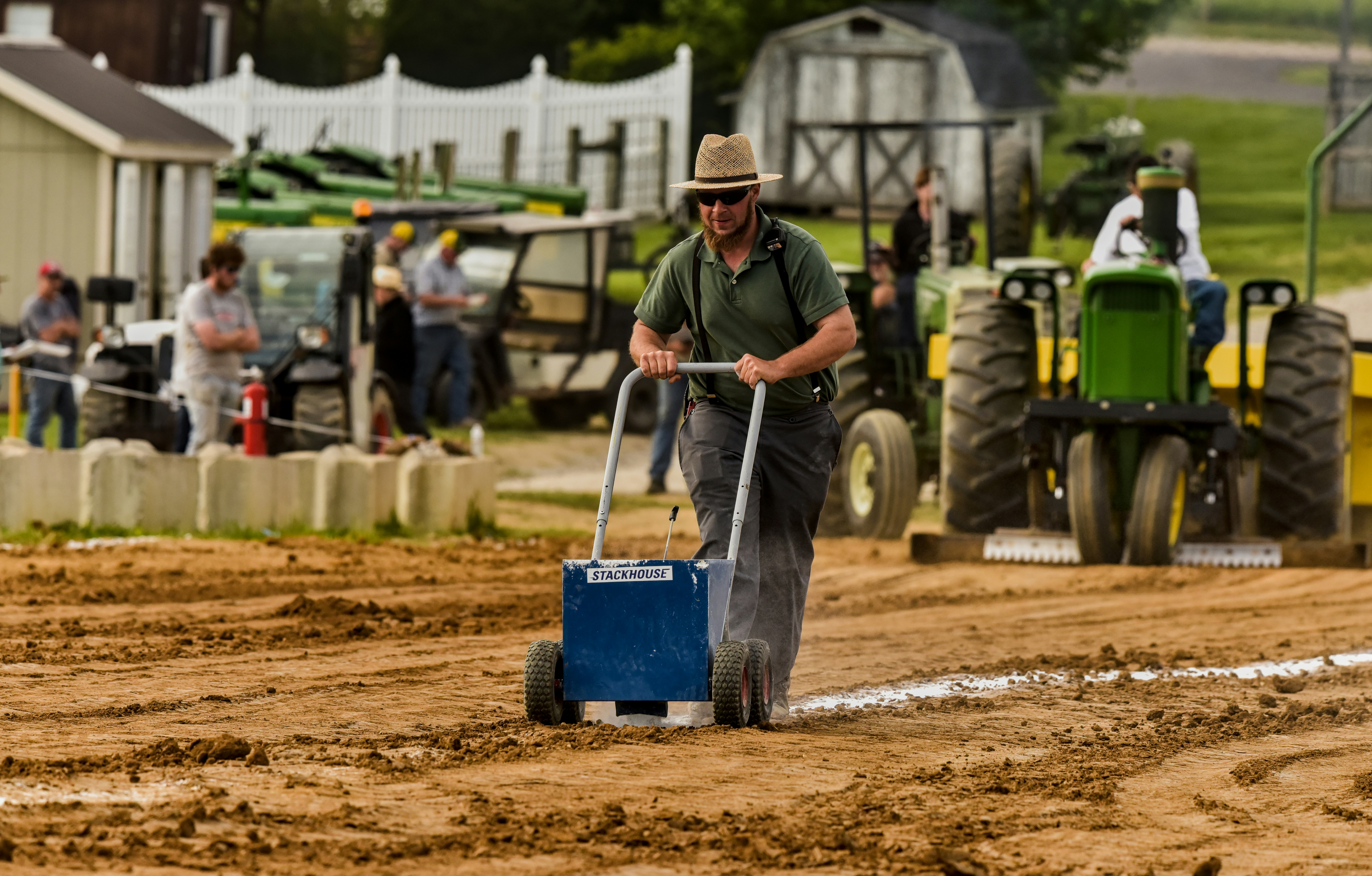 Man in hat pushing line marker on dirt track.