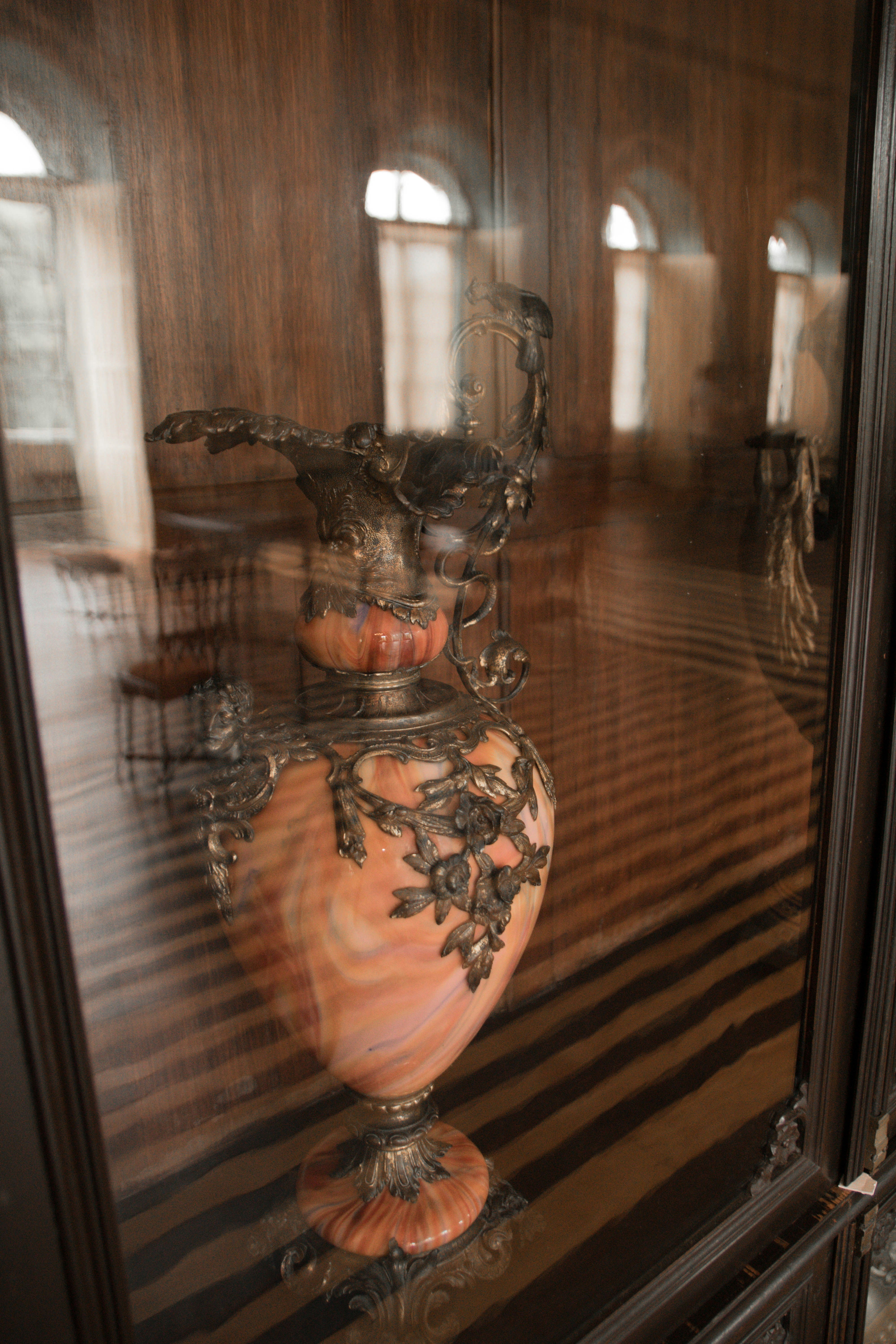 Decorative marble urn with metal details behind reflective glass.