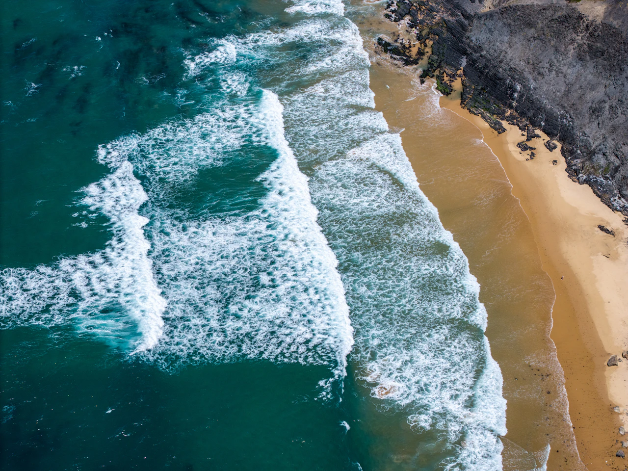 Ocean waves meeting a sandy shore and rocky coastline