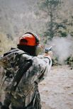Person in camouflage firing a handgun outdoors with muzzle flash.