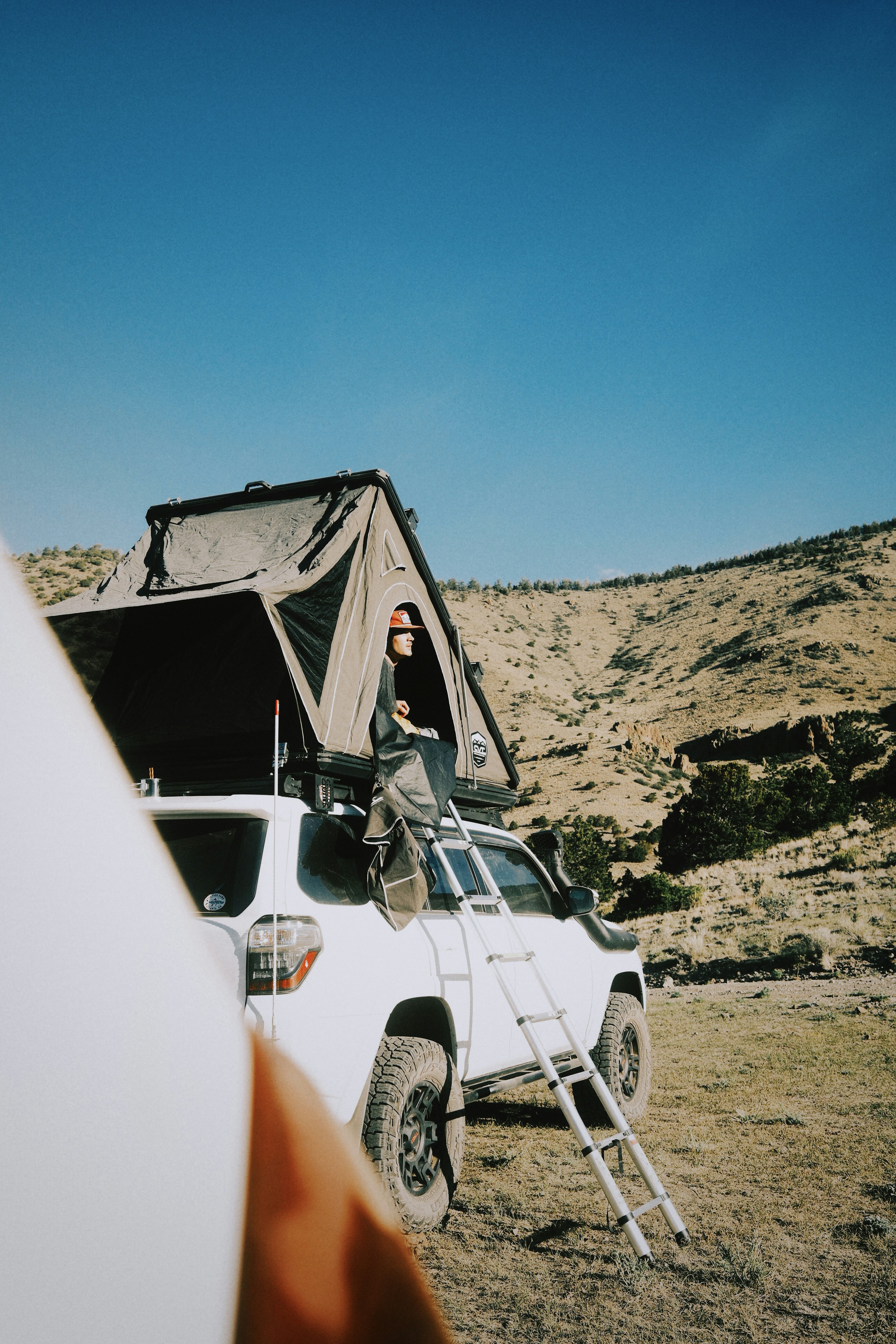 Man setting up rooftop tent on suv in dry hills.