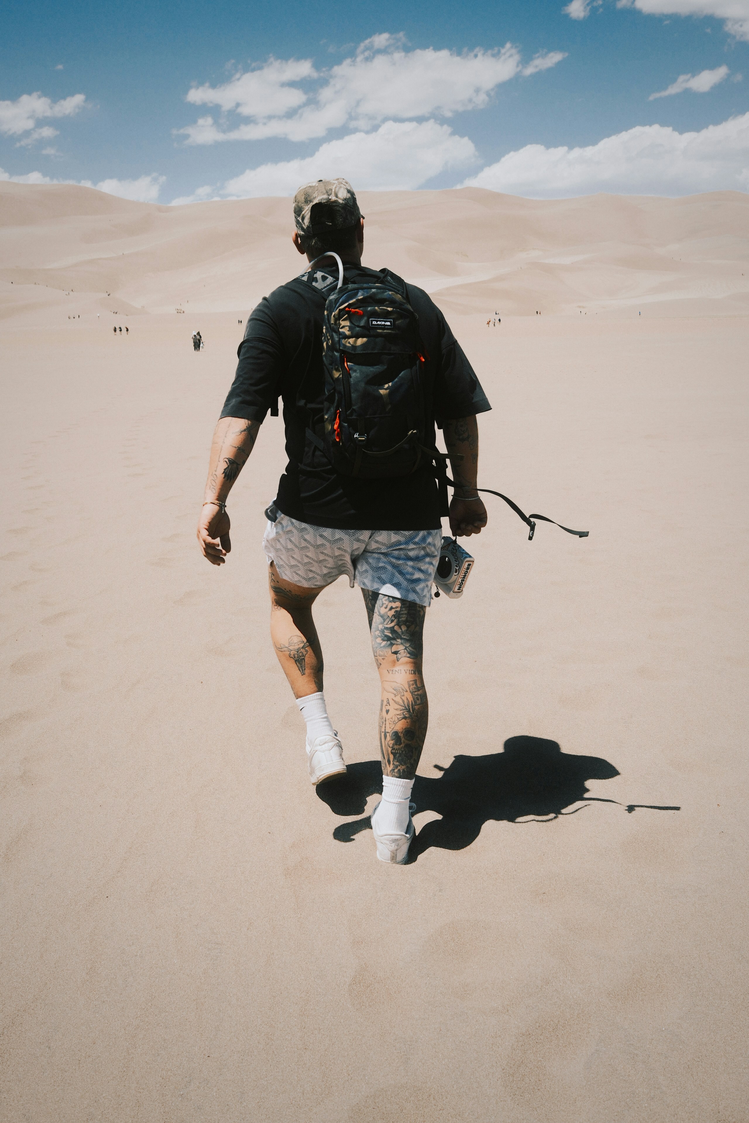 Homem com mochila fazendo trilhas por dunas de areia no deserto.