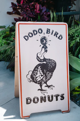 Dodo bird donuts sign with cartoon dodo and foliage.