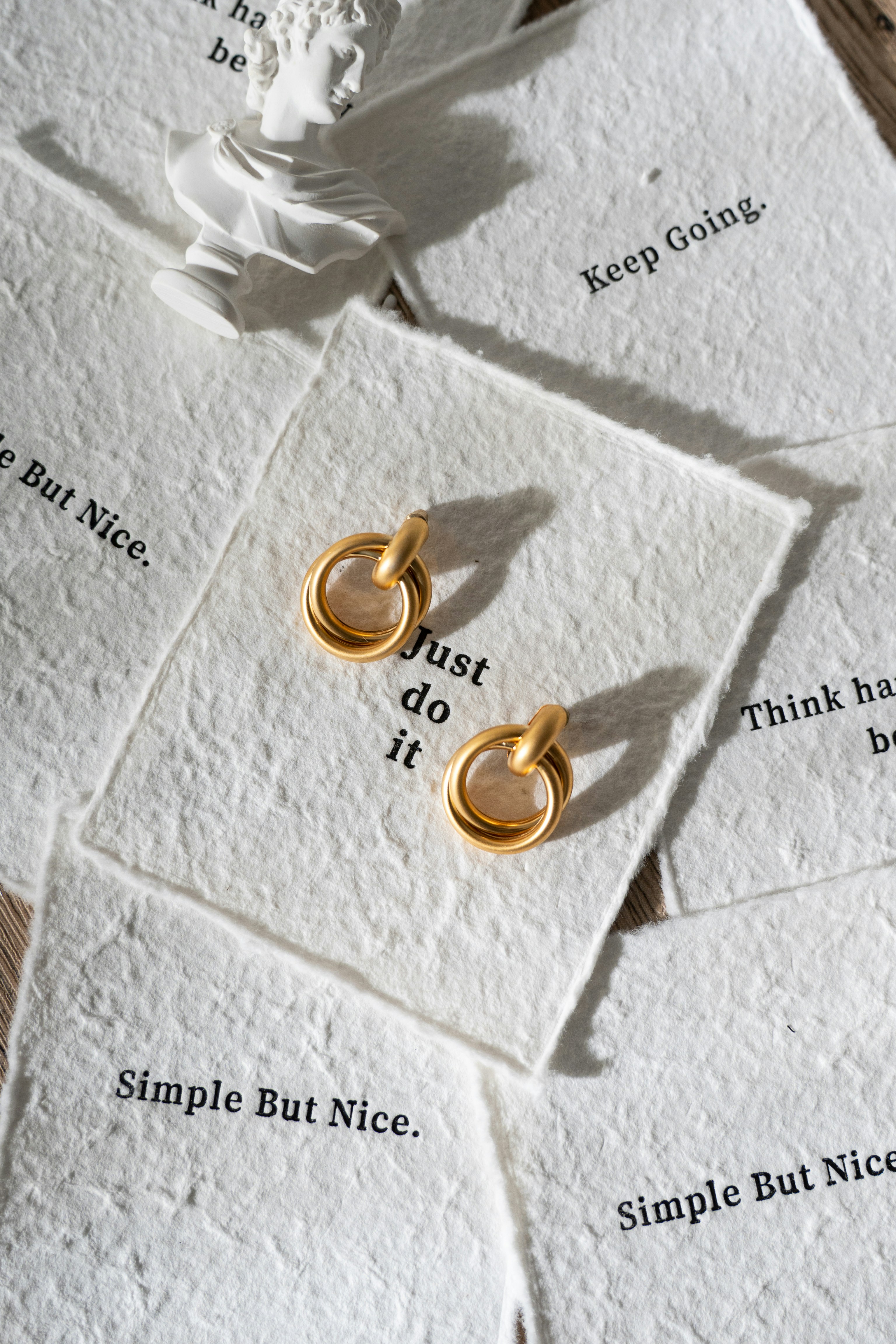 Gold hoop earrings on textured cards with motivational quotes