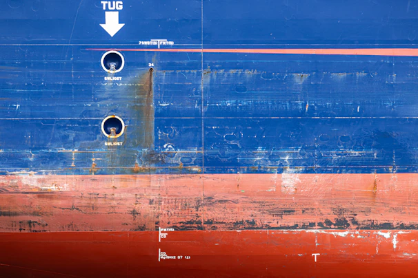 Weathered blue and red ship hull with markings and rust.
