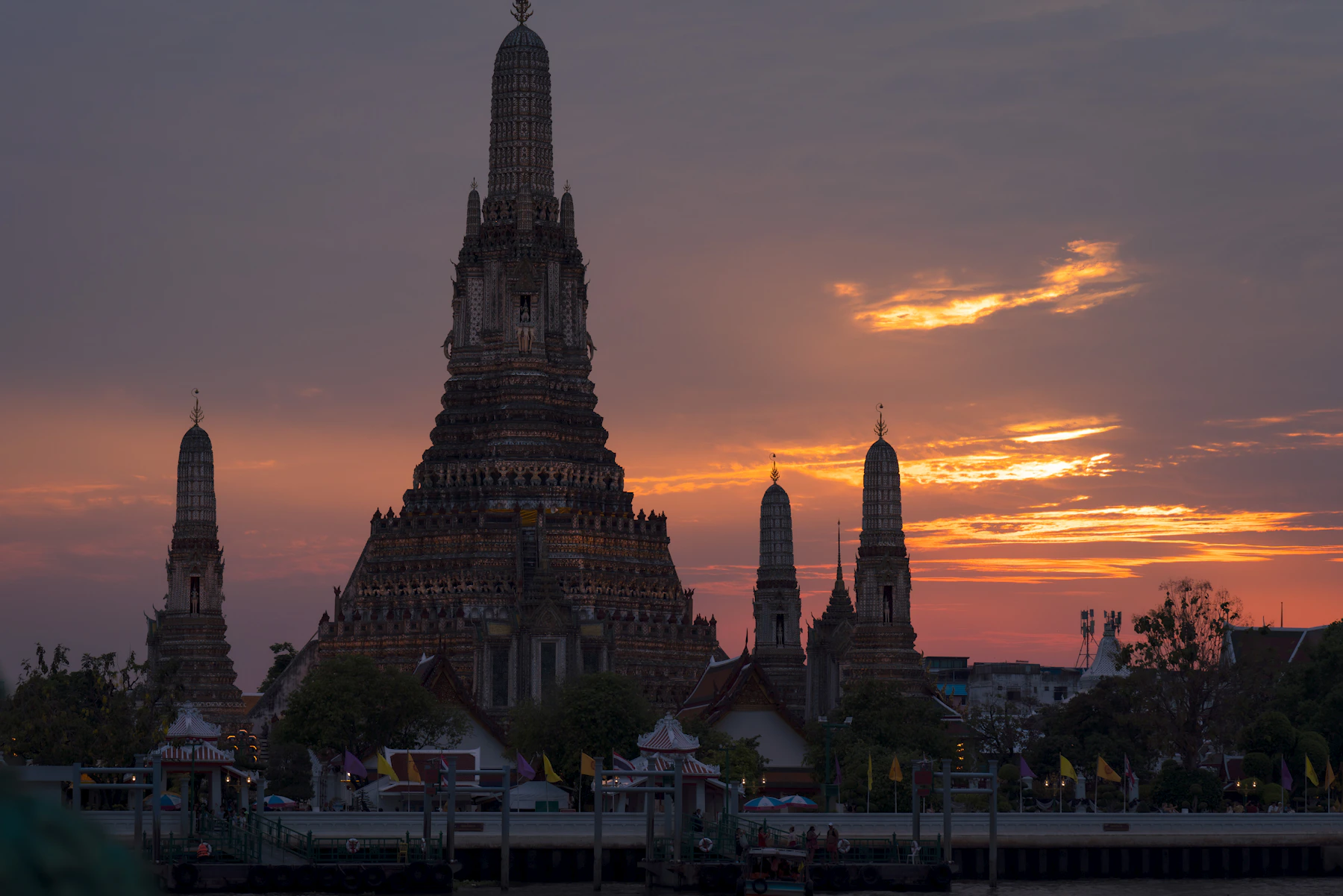 Wat Arun silhouetted beside the Chao Phraya River at a vivid Bangkok sunset