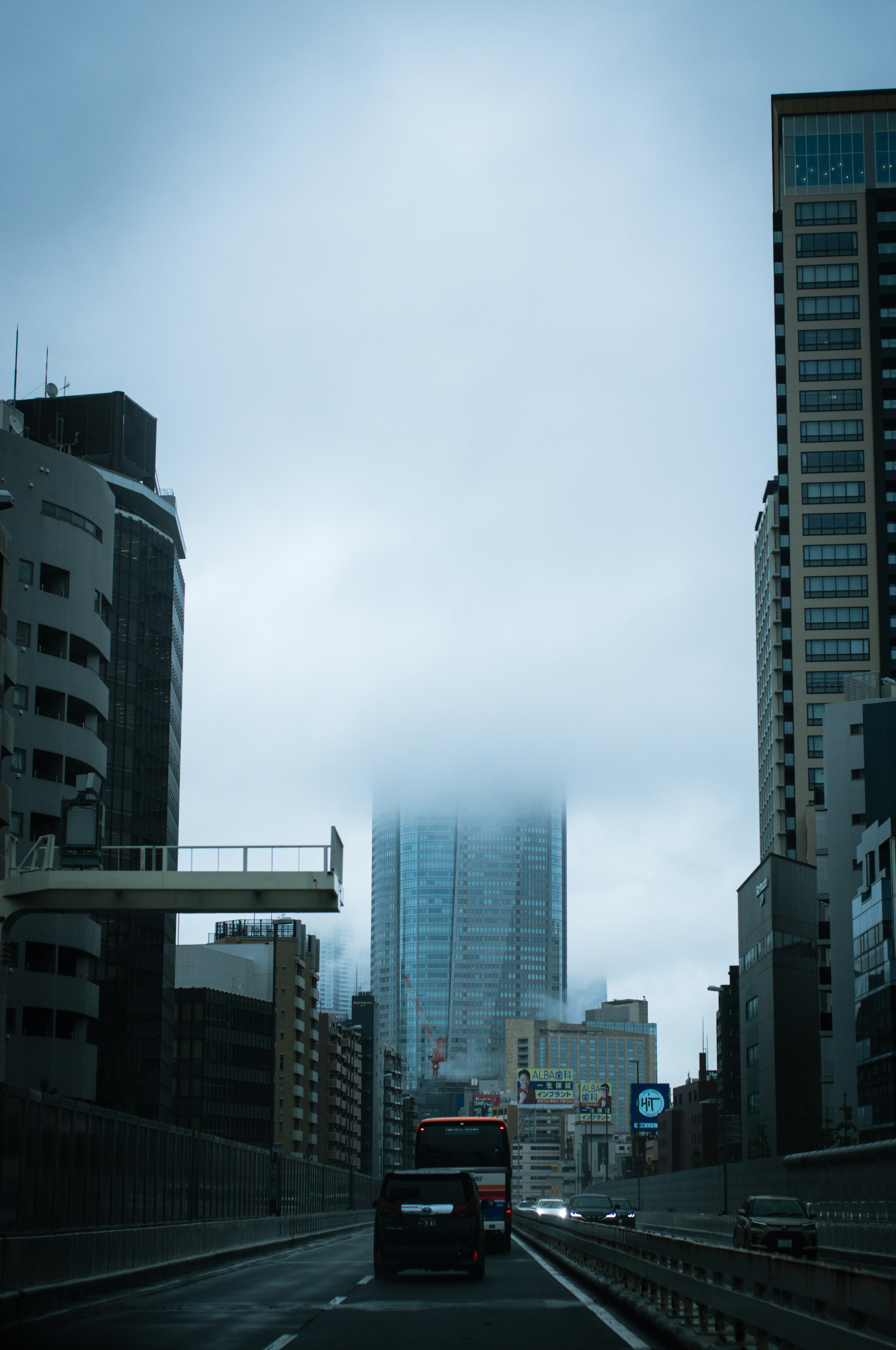 Foggy skyscraper dominates a city highway under an overcast sky.