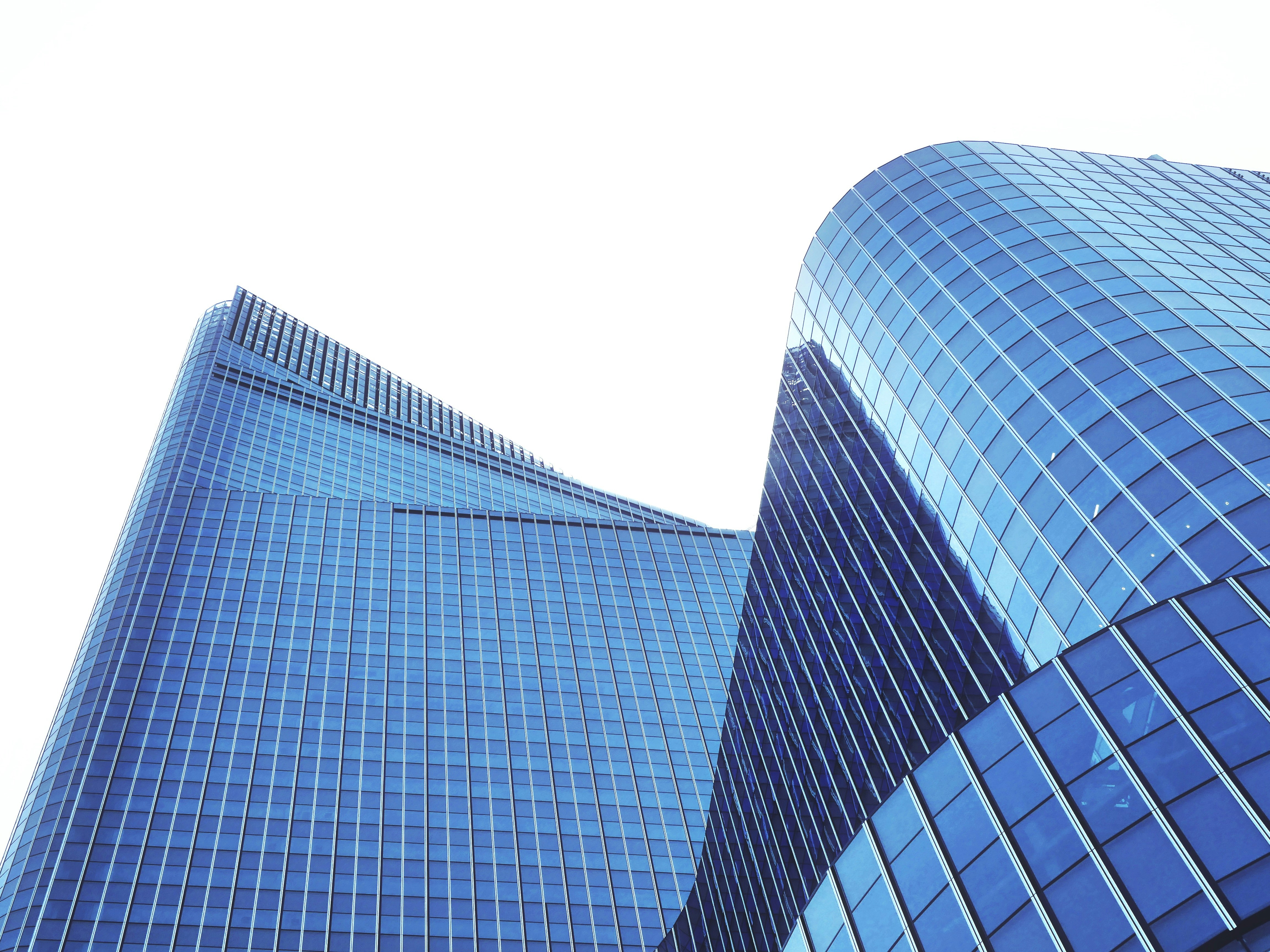 Rascacielos modernos de cristal azul con arquitectura curva contra cielo blanco.