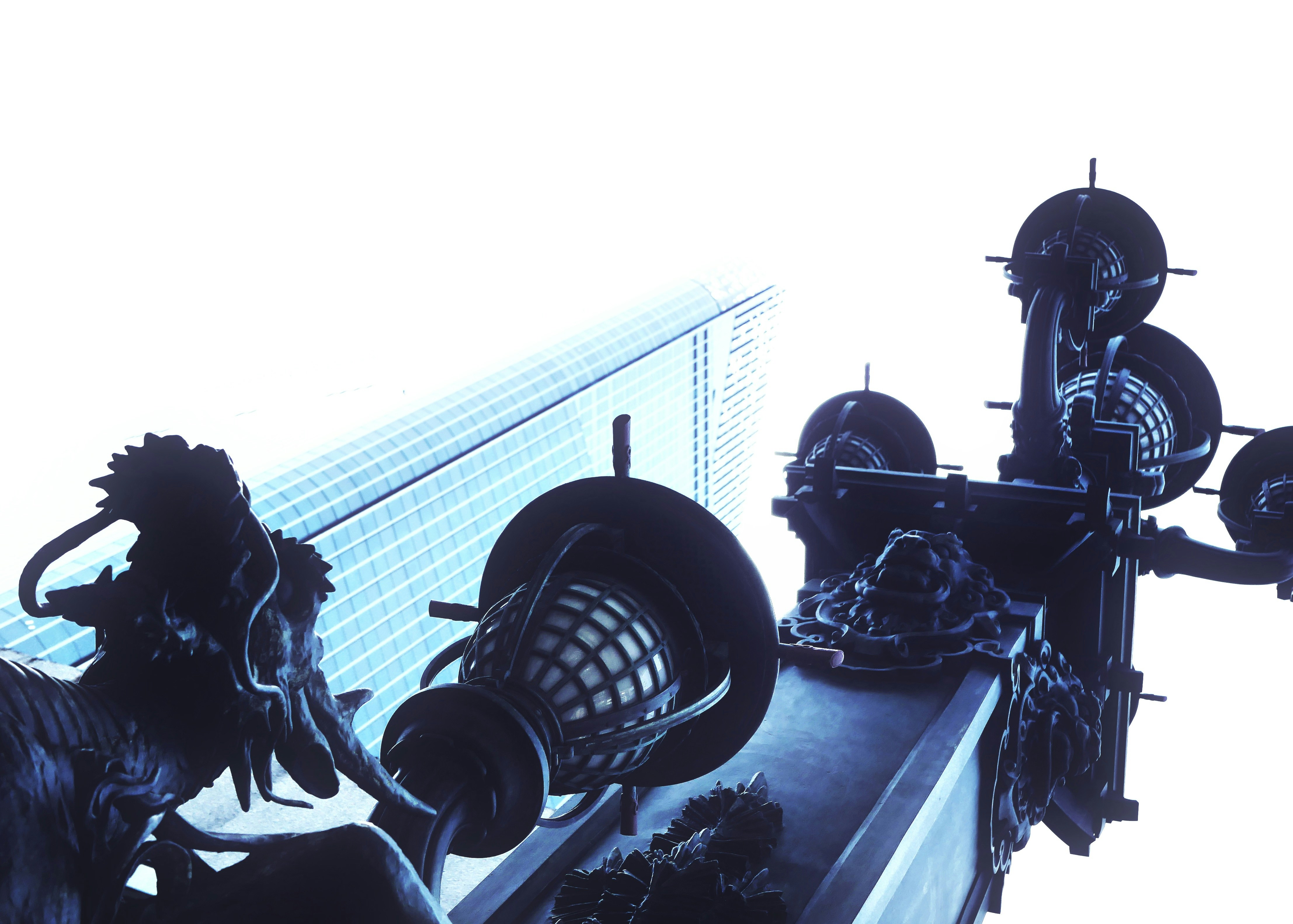 Esculturas oscuras y ornamentadas contra un edificio moderno y un cielo blanco.