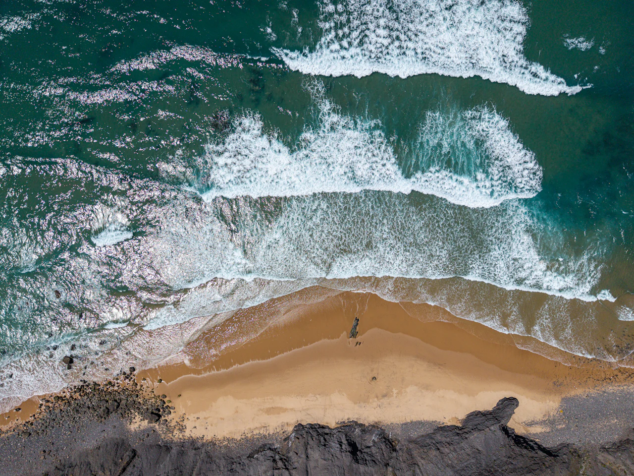 Ocean waves crashing on a sandy beach with dark cliffs