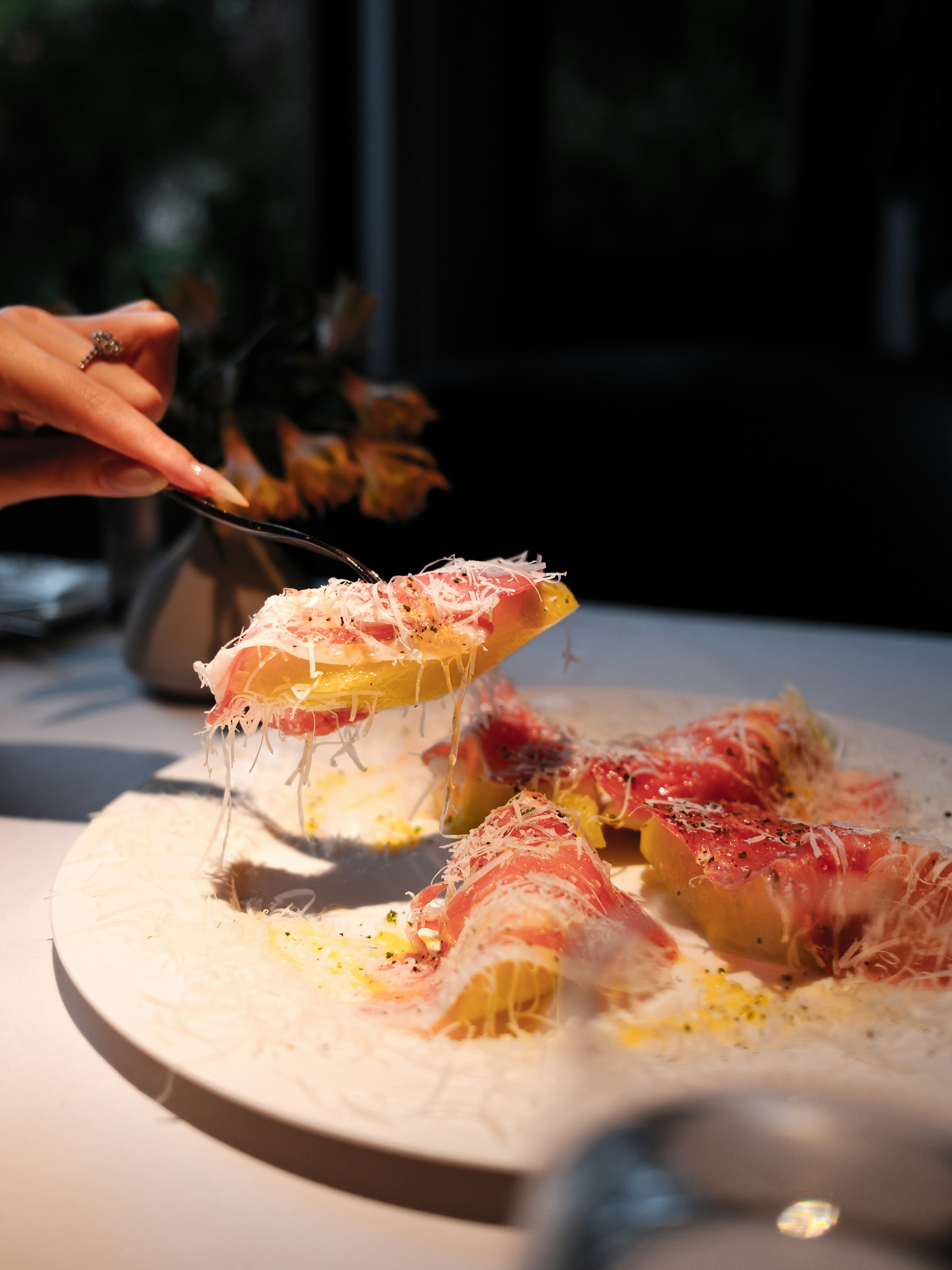Hand lifting gourmet dish with cheese and prosciutto