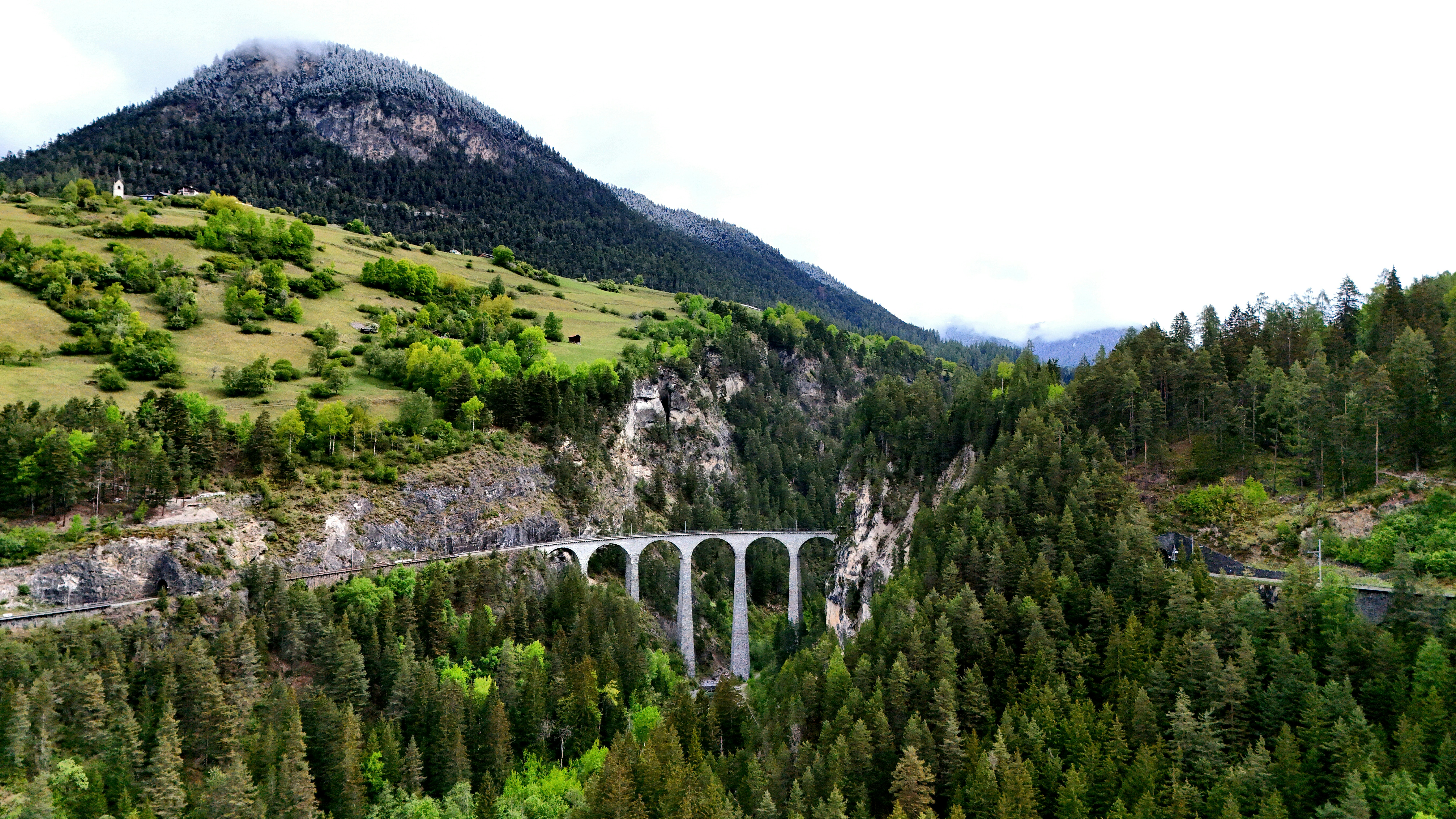 Viaduto histórico de pedra que atravessa um vale montanhoso arborizado.