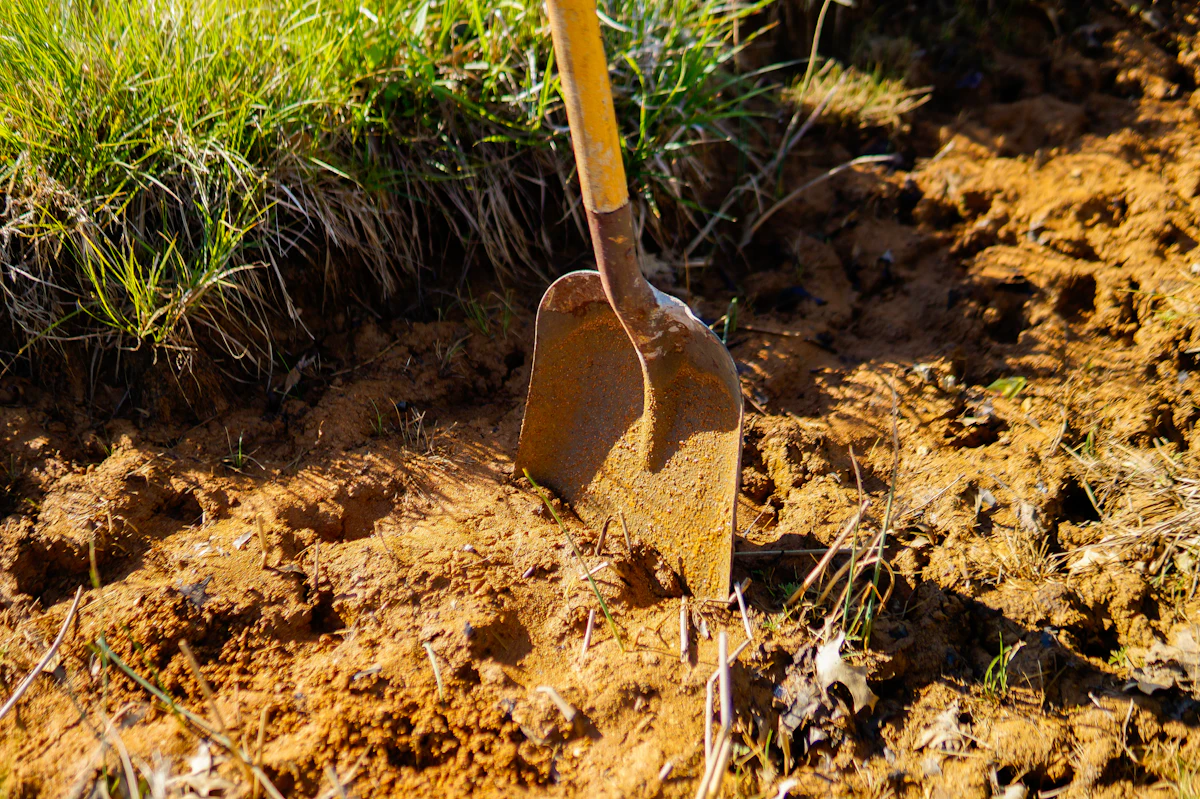 A garden shovel driven into dark brown soil