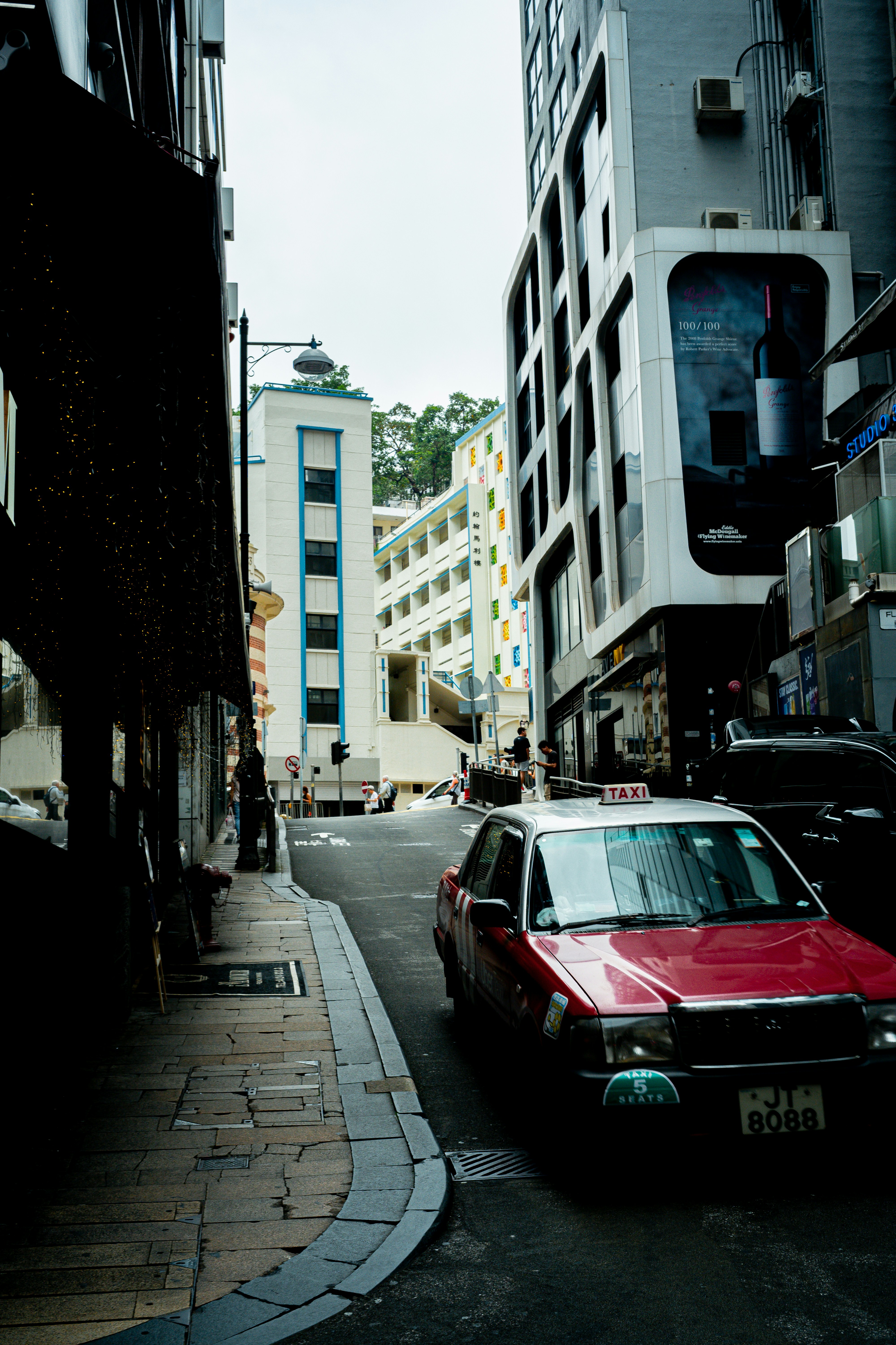Red taxi on a narrow city street with tall buildings.