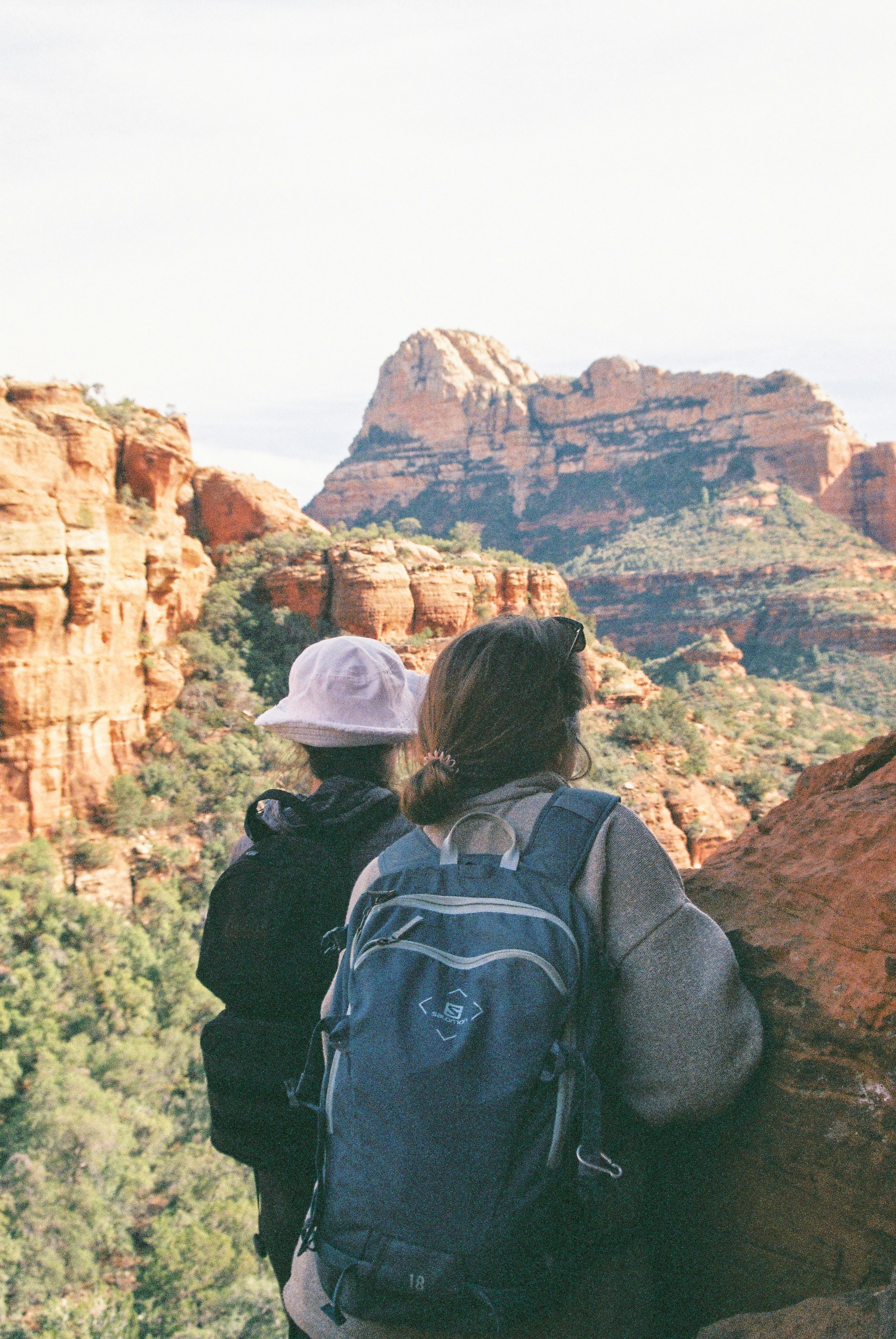 Two people hiking, admiring red rock mountains from a viewpoint.