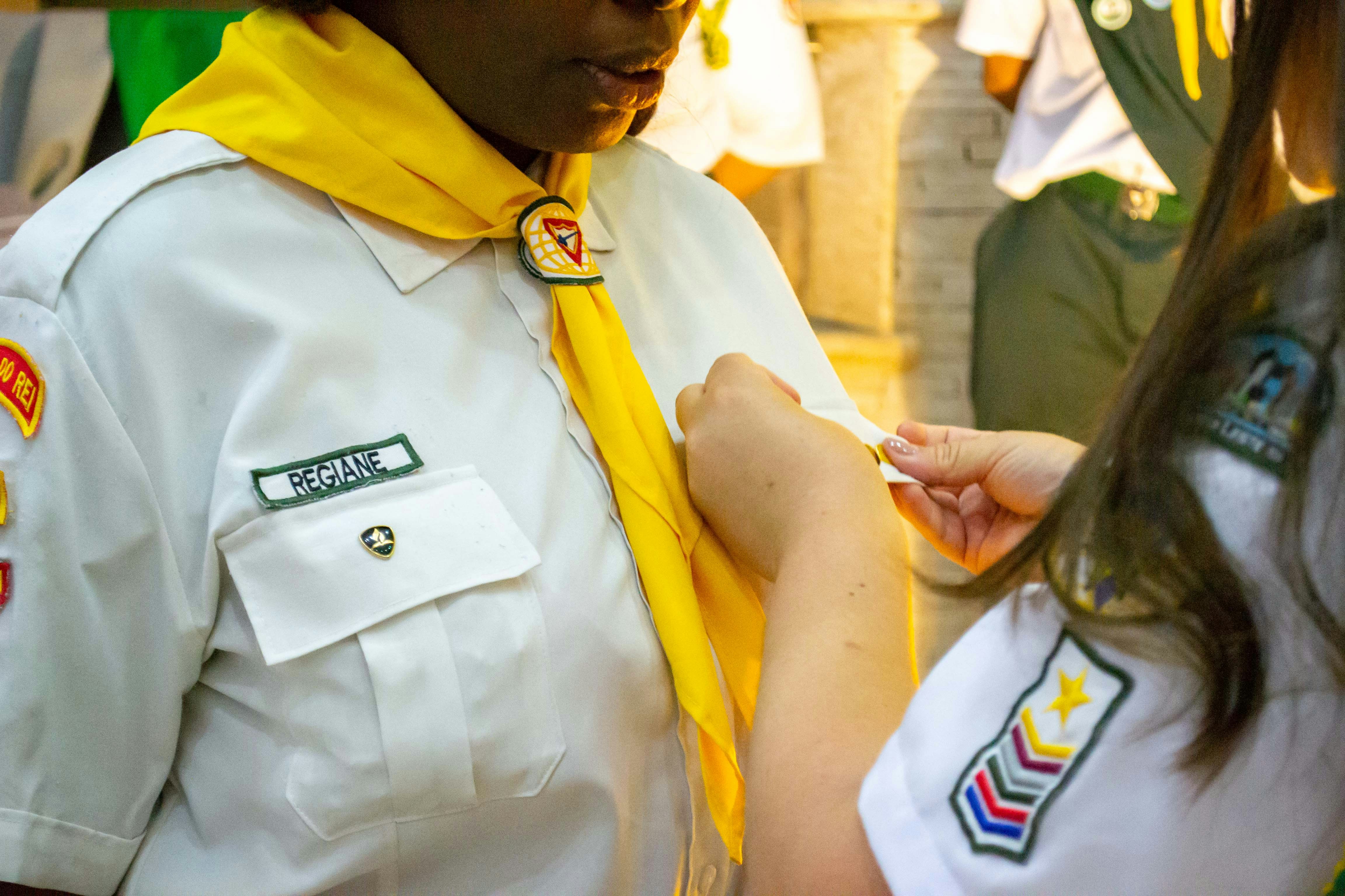 Two people in scout uniforms adjusting a badge.