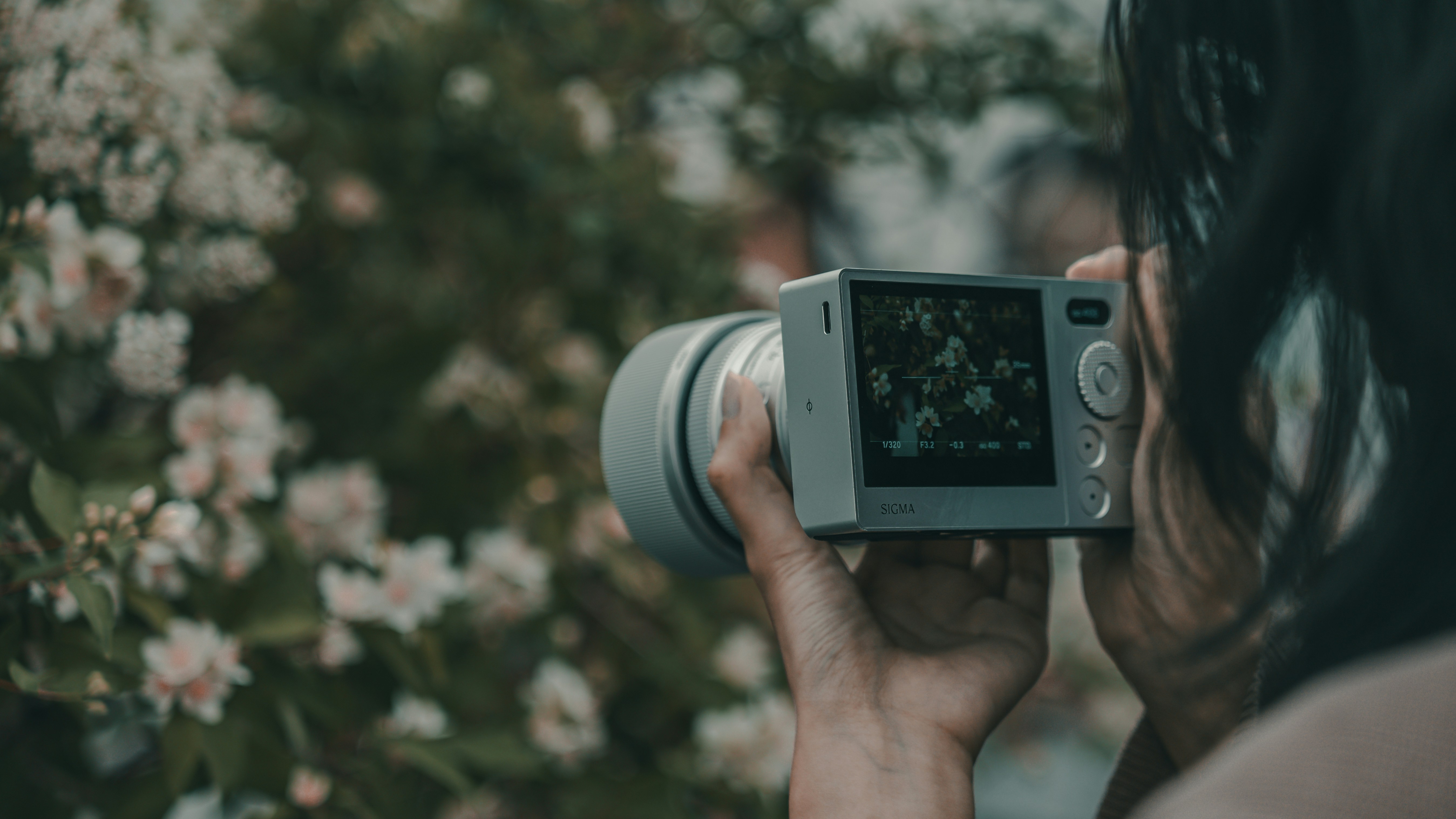 Woman holding a digital camera photographing white flowers.