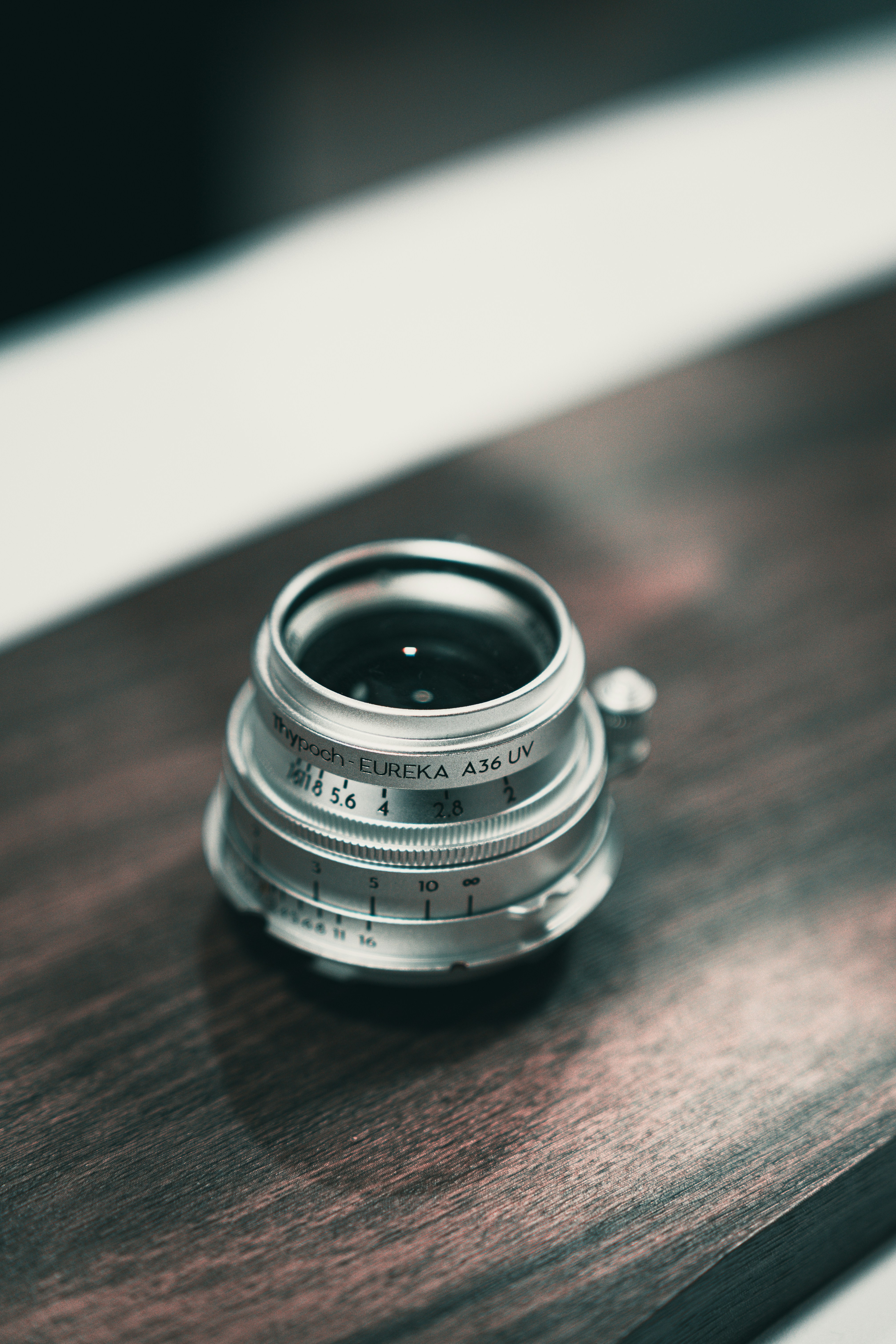 A vintage camera lens sits on a dark wooden surface.