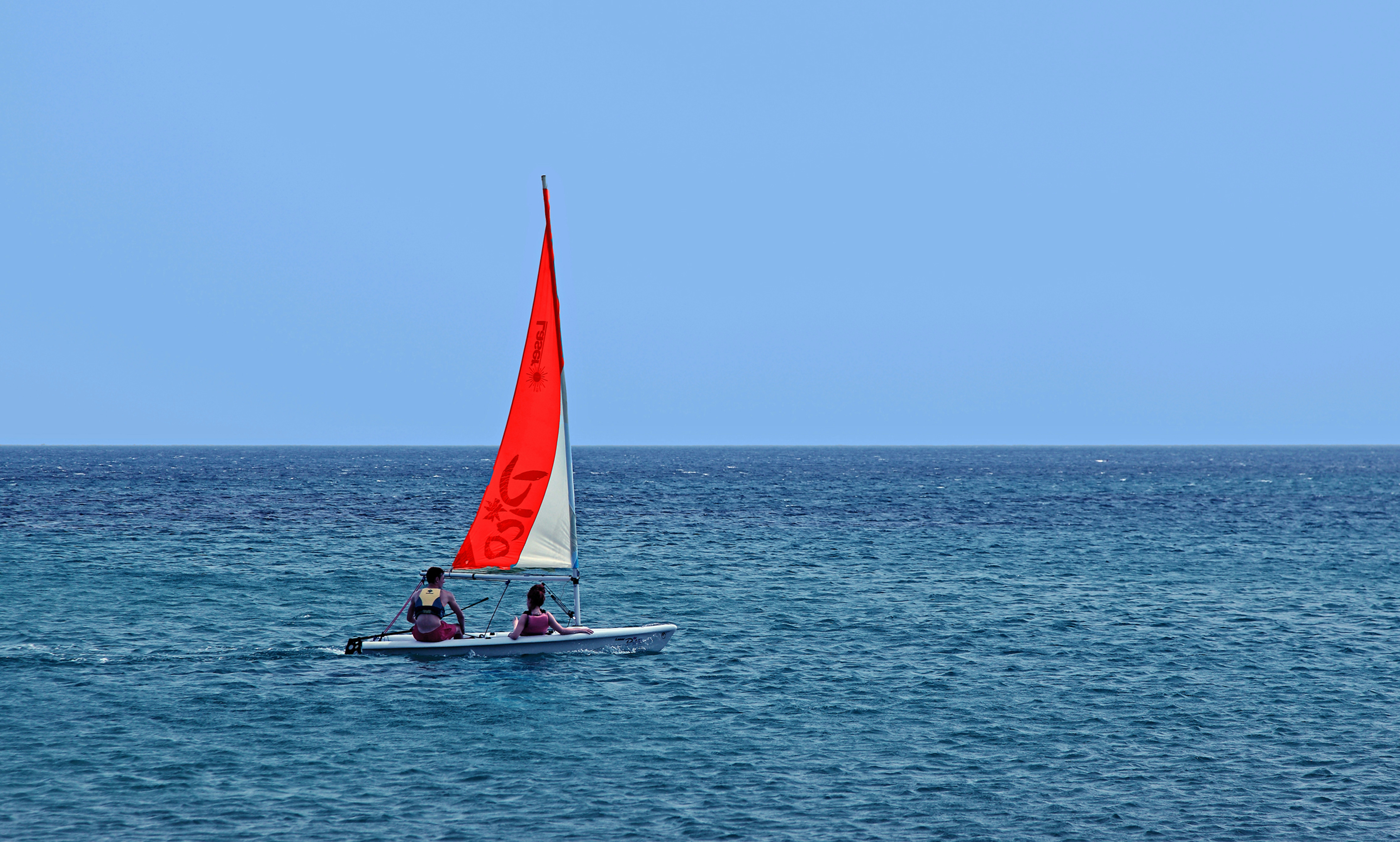 Piccola barca a vela con vela rossa su oceano blu.