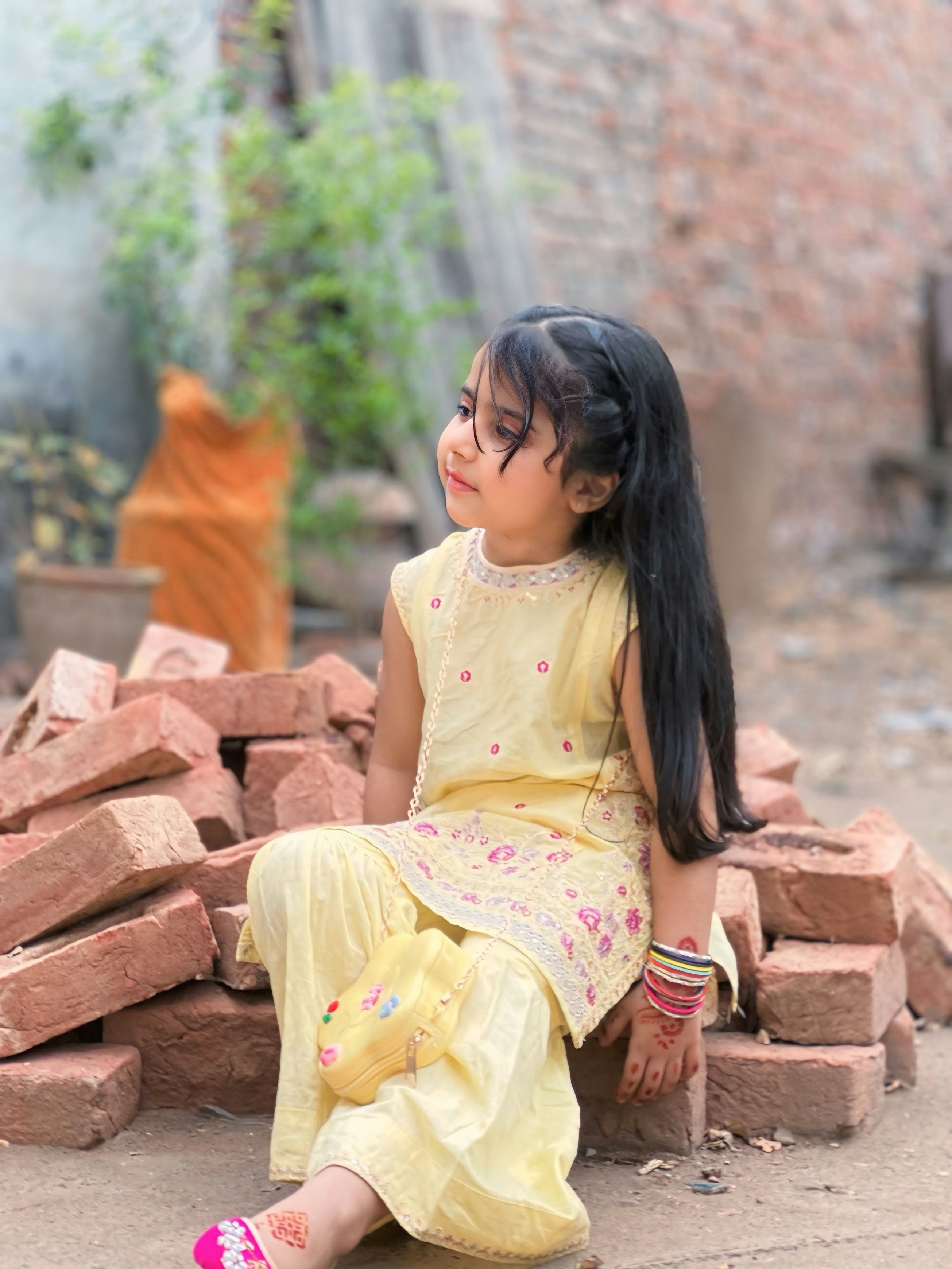 Une jeune fille en tenue jaune assise sur des briques