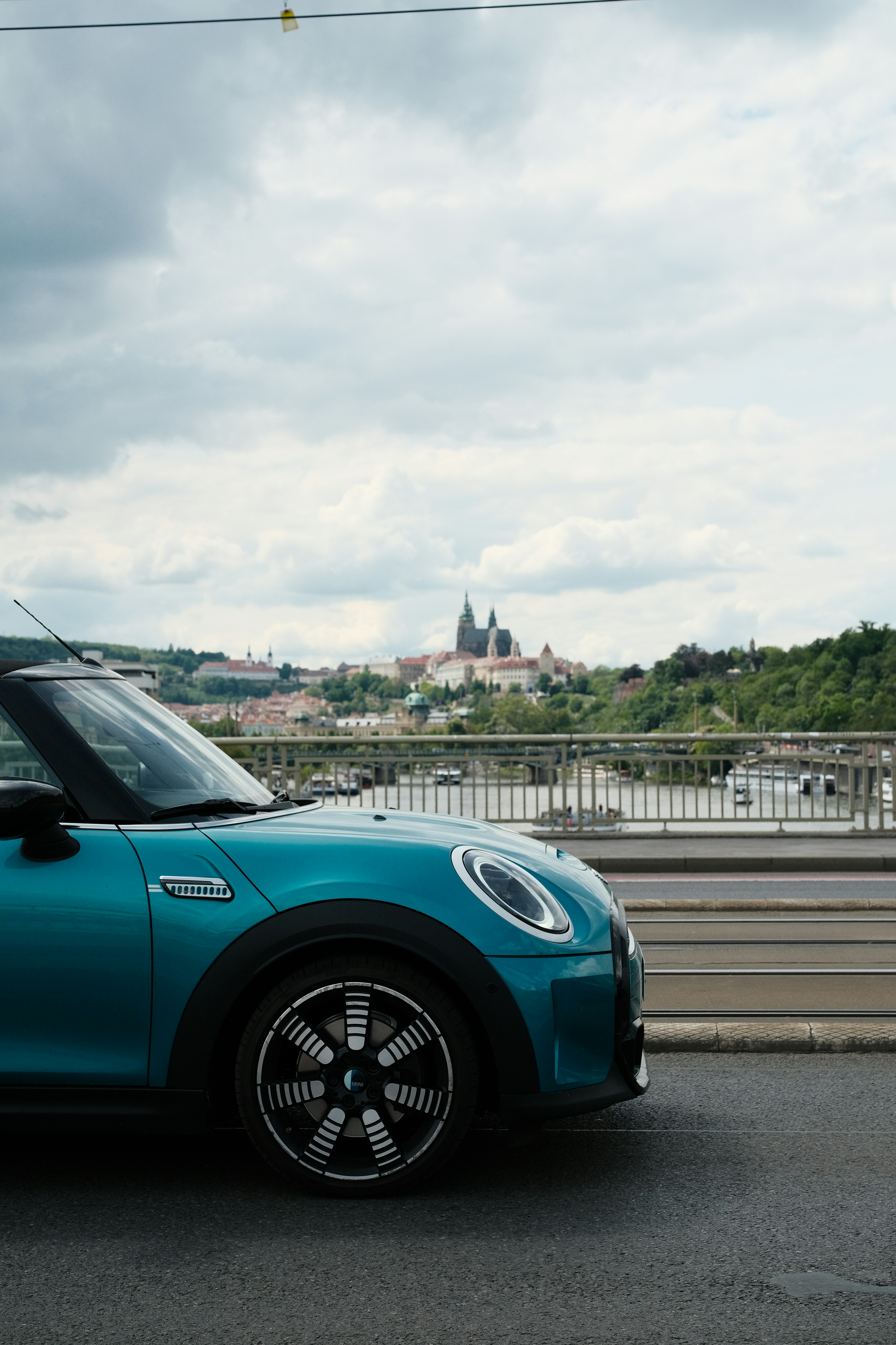 Mini tonelera turquesa en un puente con un castillo lejano.