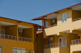 Two yellow buildings with balconies under a clear blue sky.