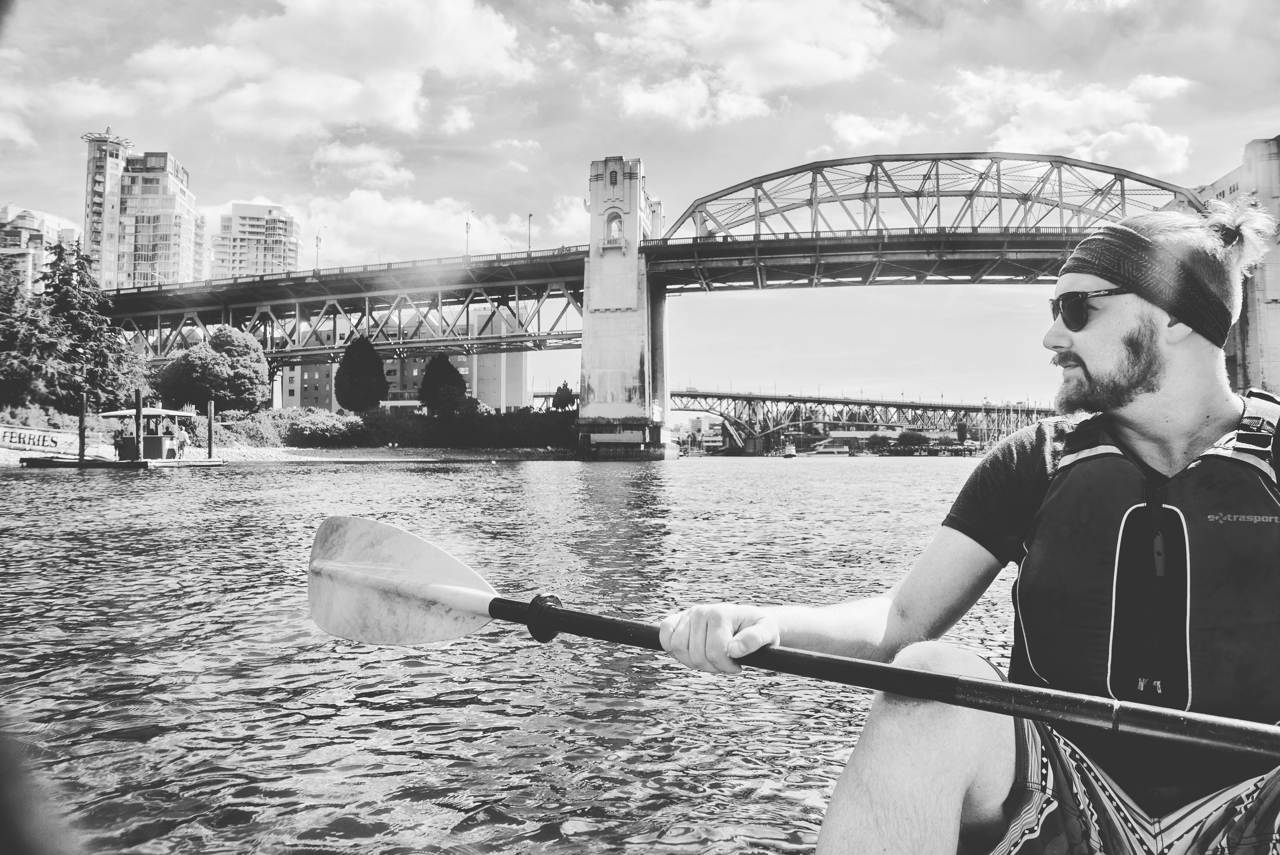 Man paddling a boat on river with city skyline.