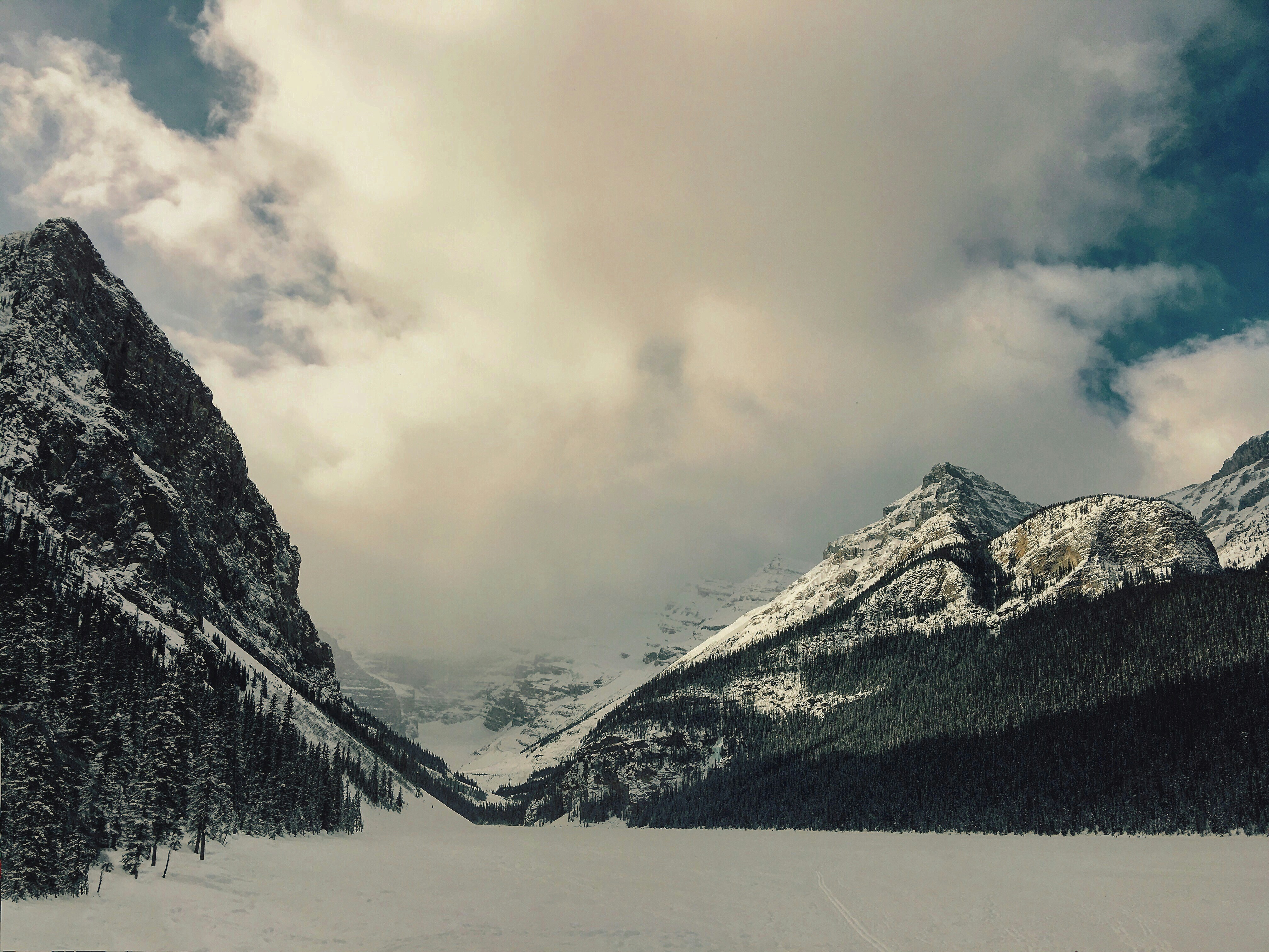 Snow-covered mountains surround a frozen lake under a cloudy sky.