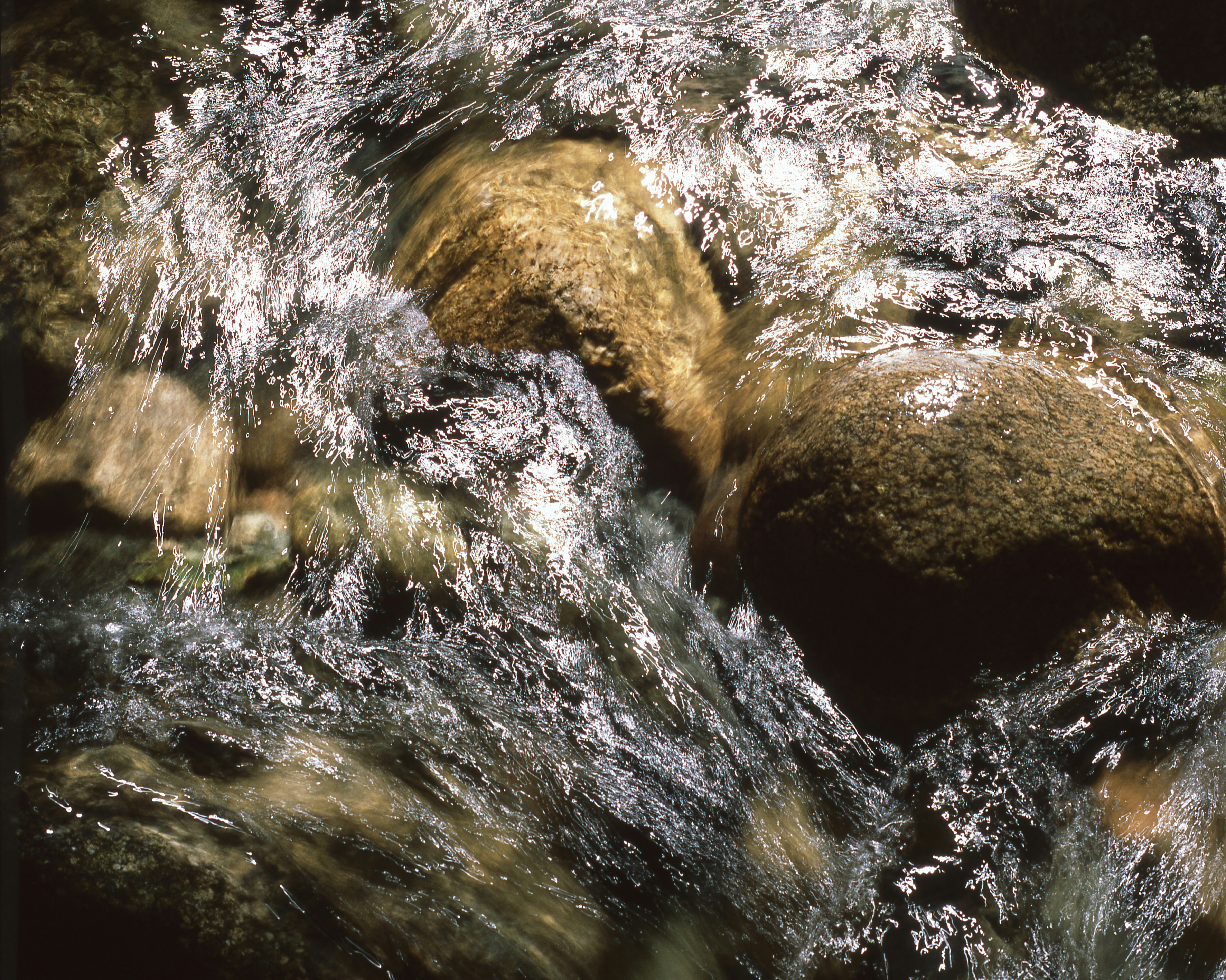 Water flowing rapidly over smooth, brown rocks.