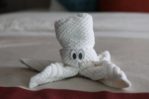 A white towel animal with googly eyes on a bed.