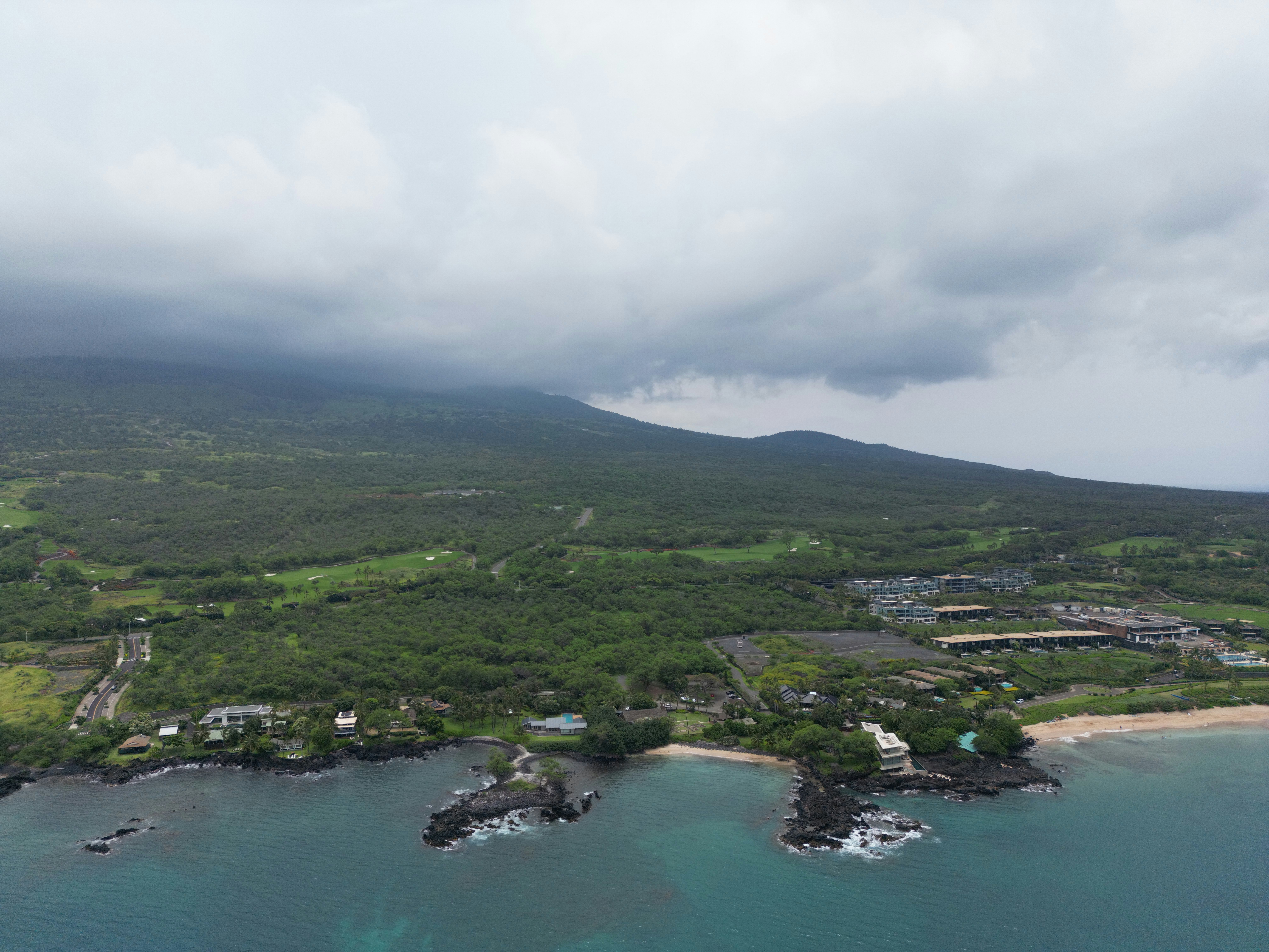 Cloudy mountain coastline with green trees and ocean.