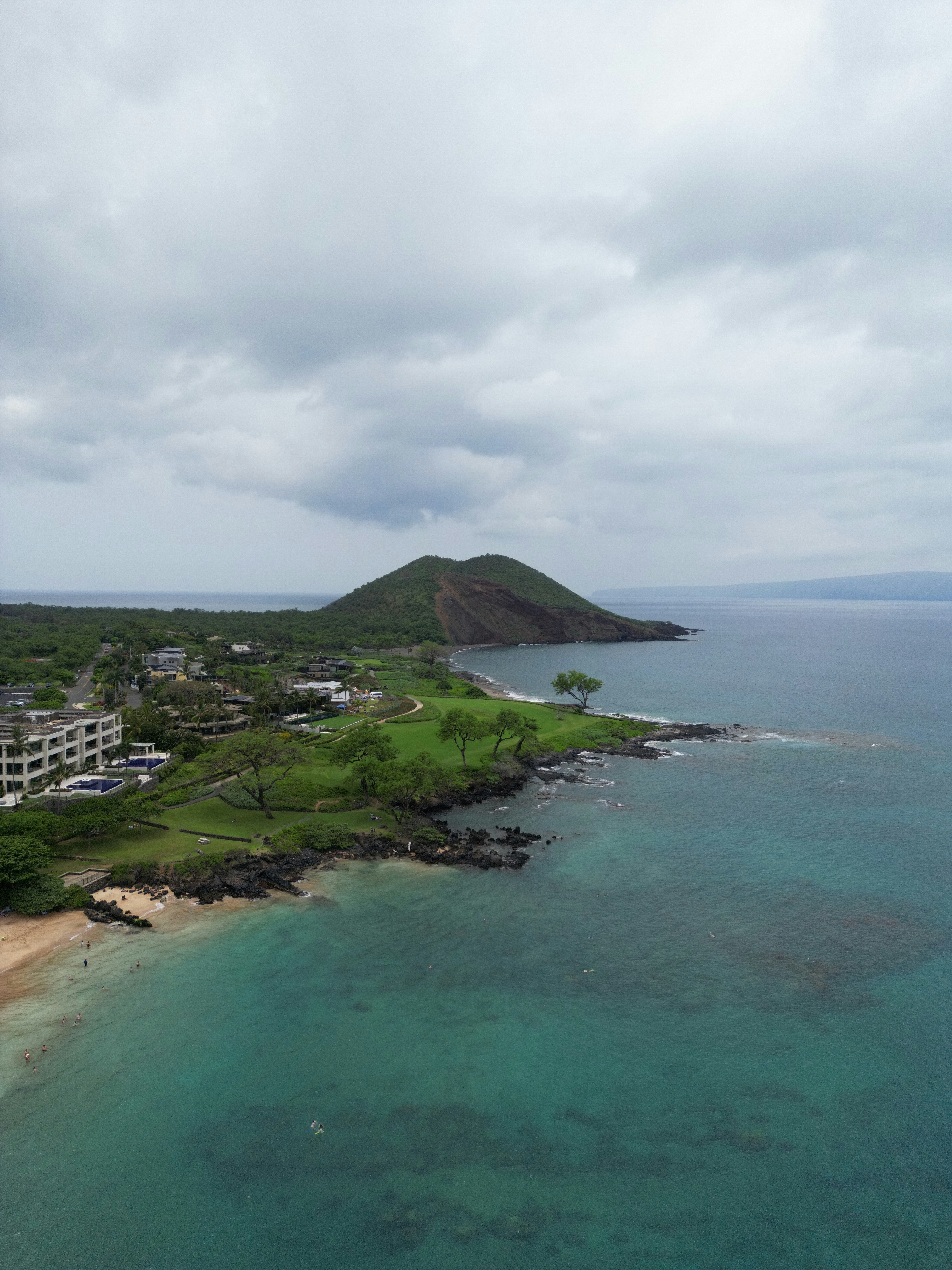 Aerial view of tropical coastline, clear ocean, and green hills.