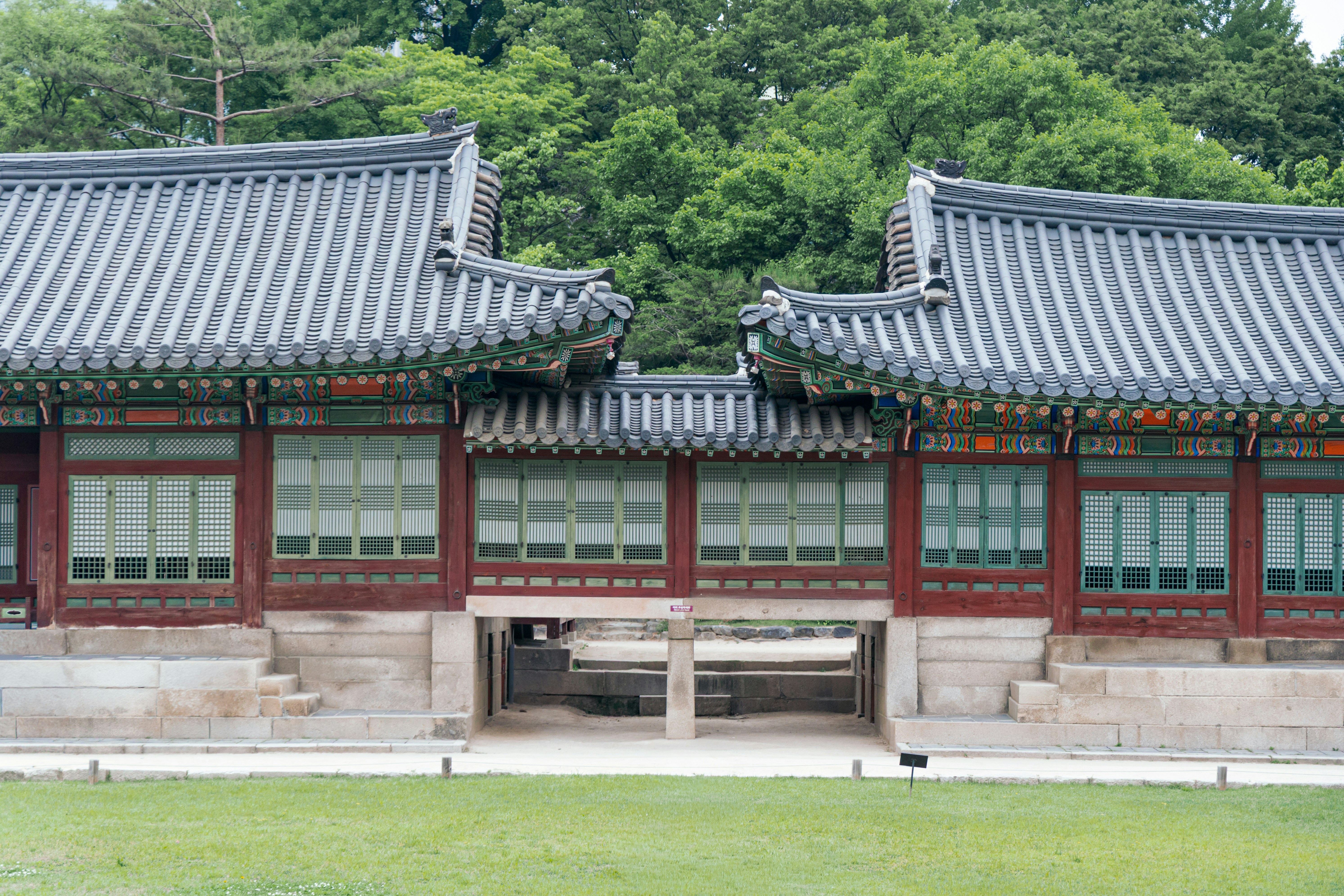 Construção tradicional de palácio coreano com árvores verdes e grama.