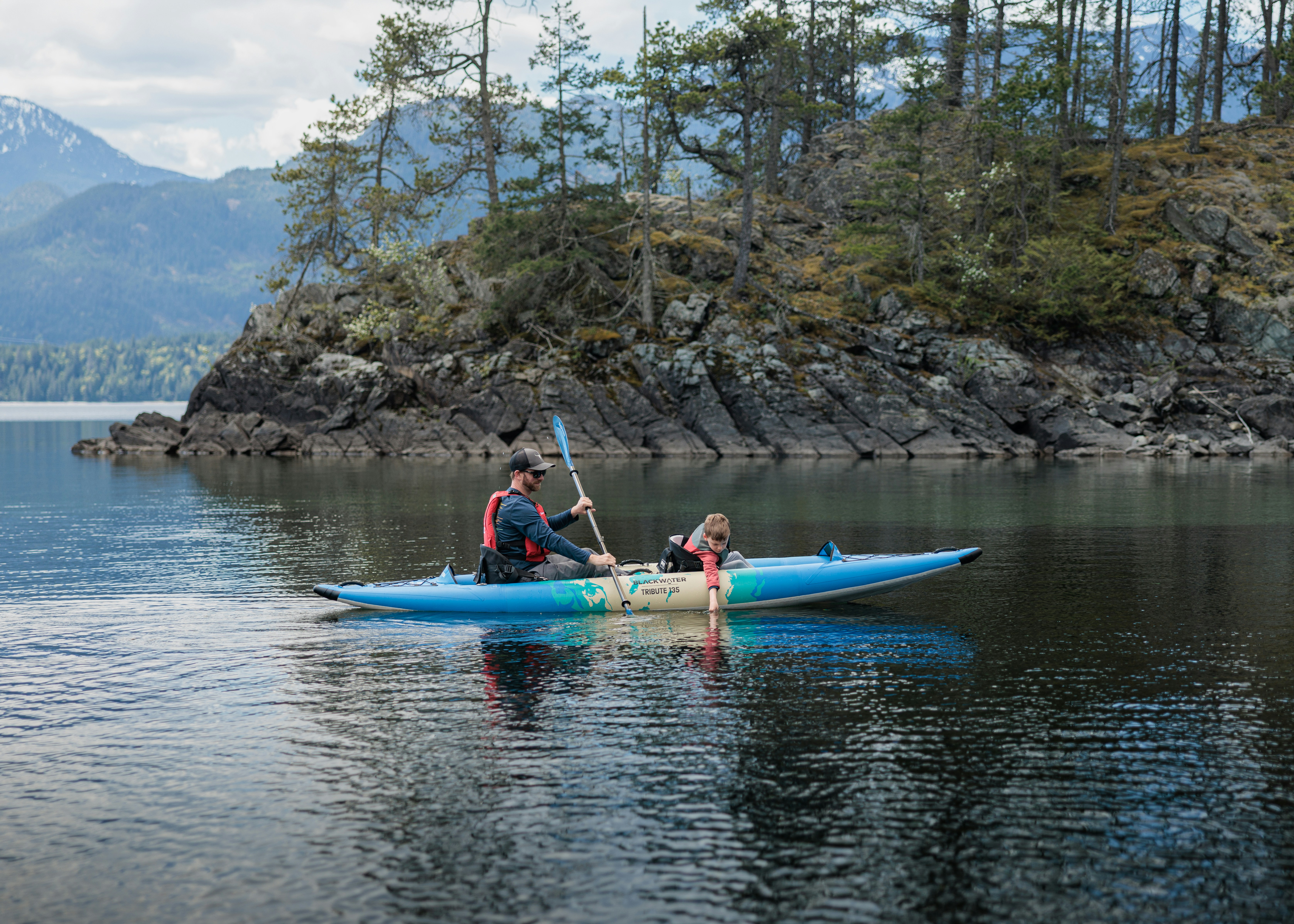 Kayakers paddle on a serene lake near a forested island.