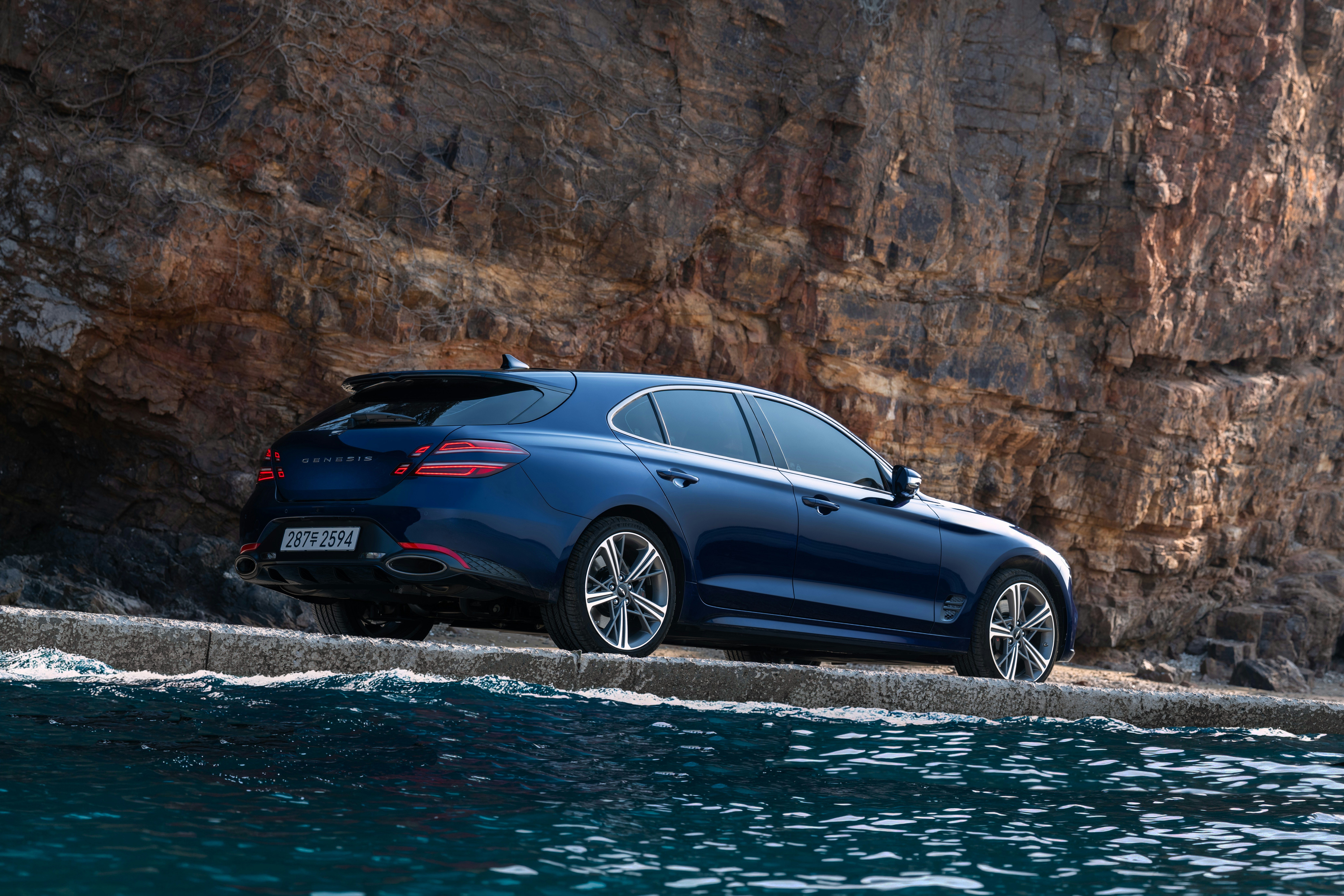 Blue car parked near rocky cliffs and water.
