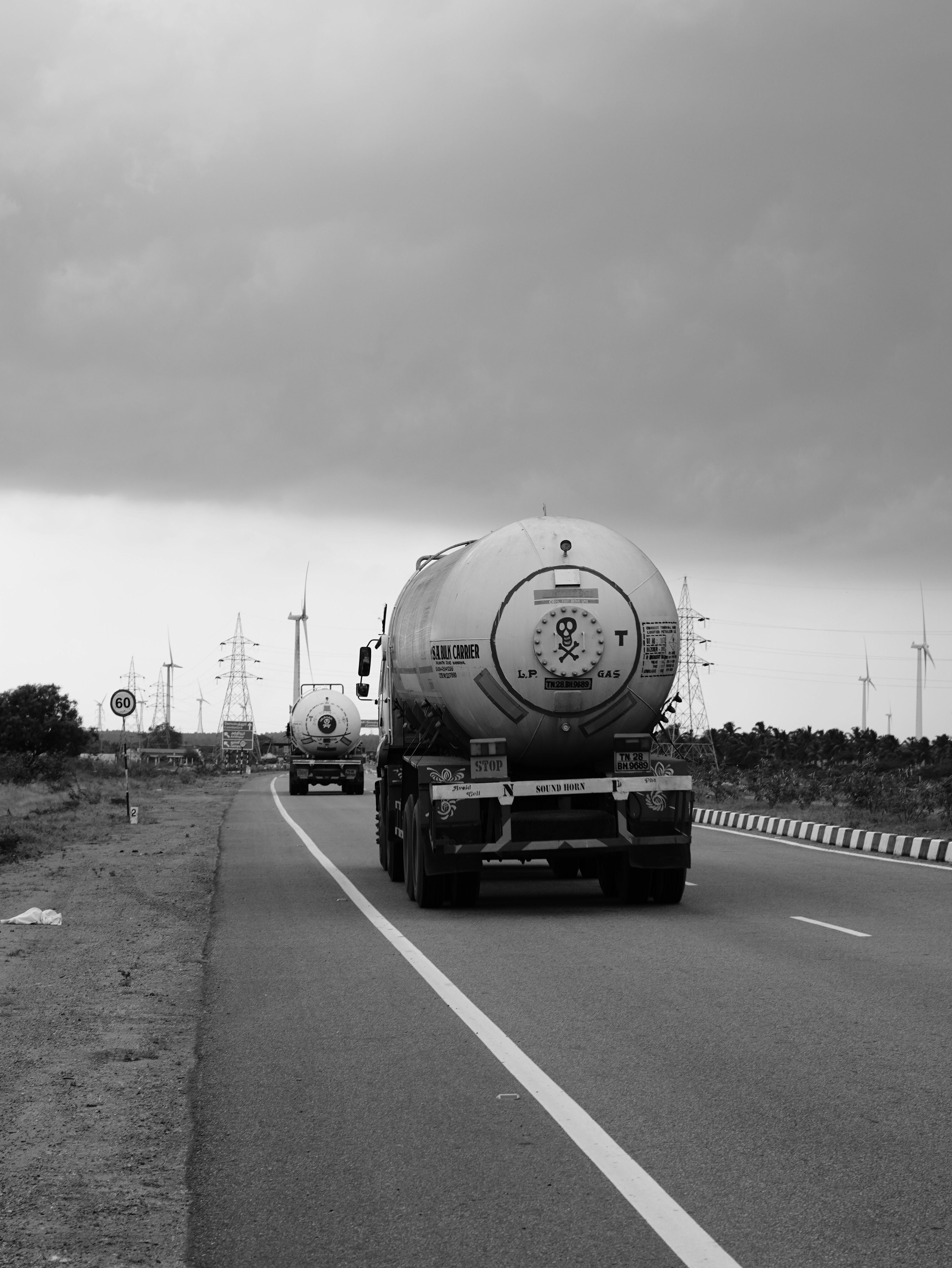 Dua truk tangki melaju di jalan raya di bawah langit mendung.