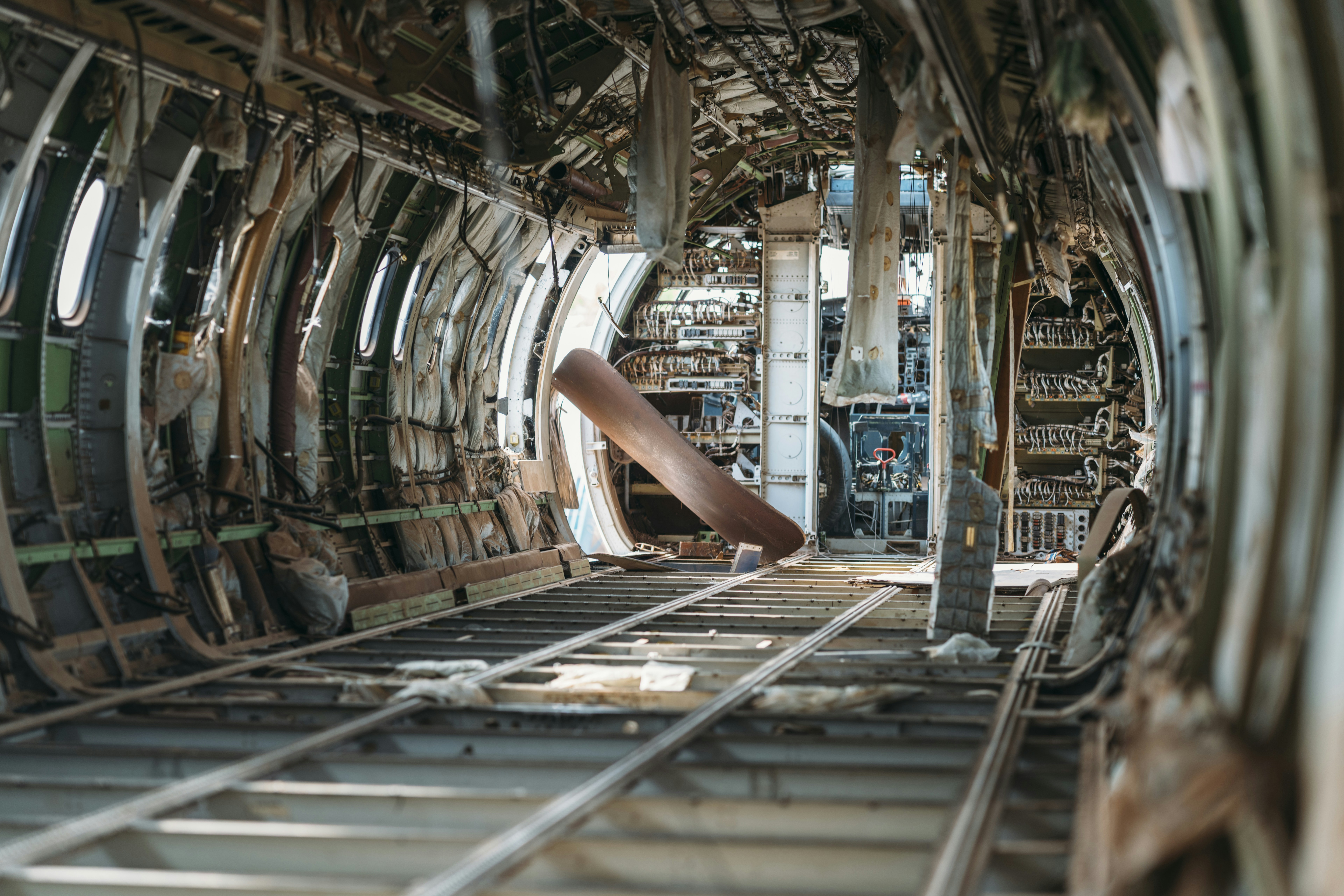 Derelict airplane fuselage interior with exposed wires and structure.