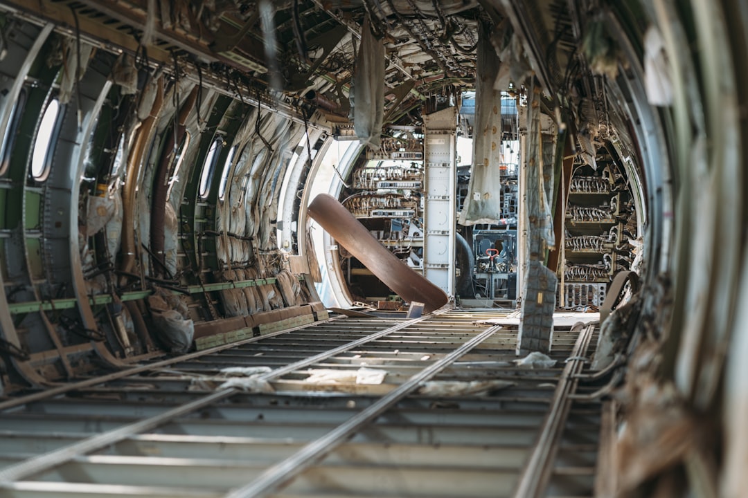 Derelict airplane fuselage interior with exposed wires and structure.